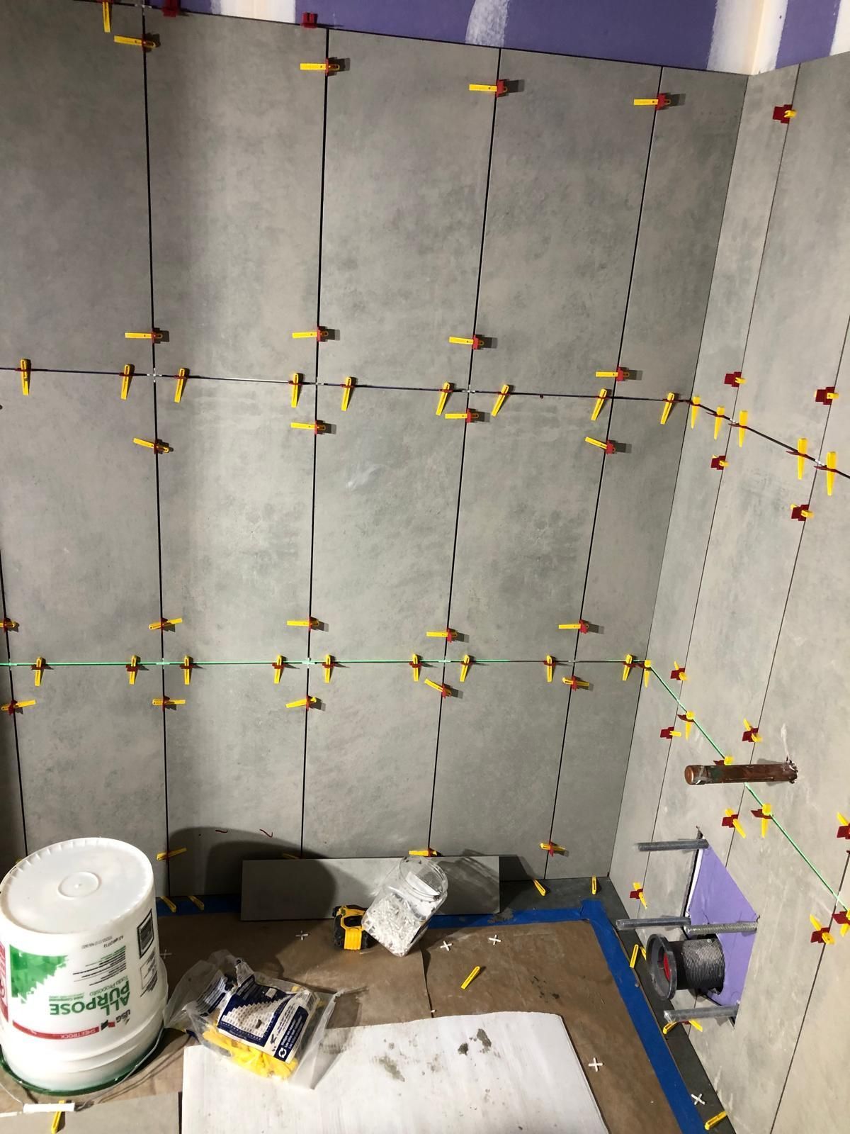 A bathroom under construction with a bucket of tile spacers on the floor.