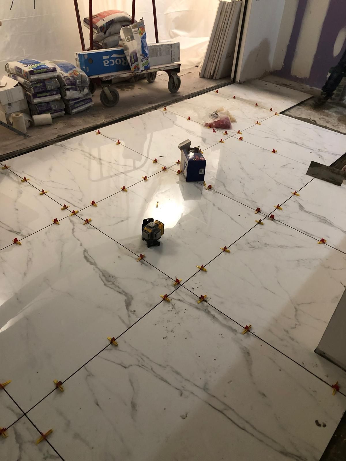 A white tile floor is being installed in a room.