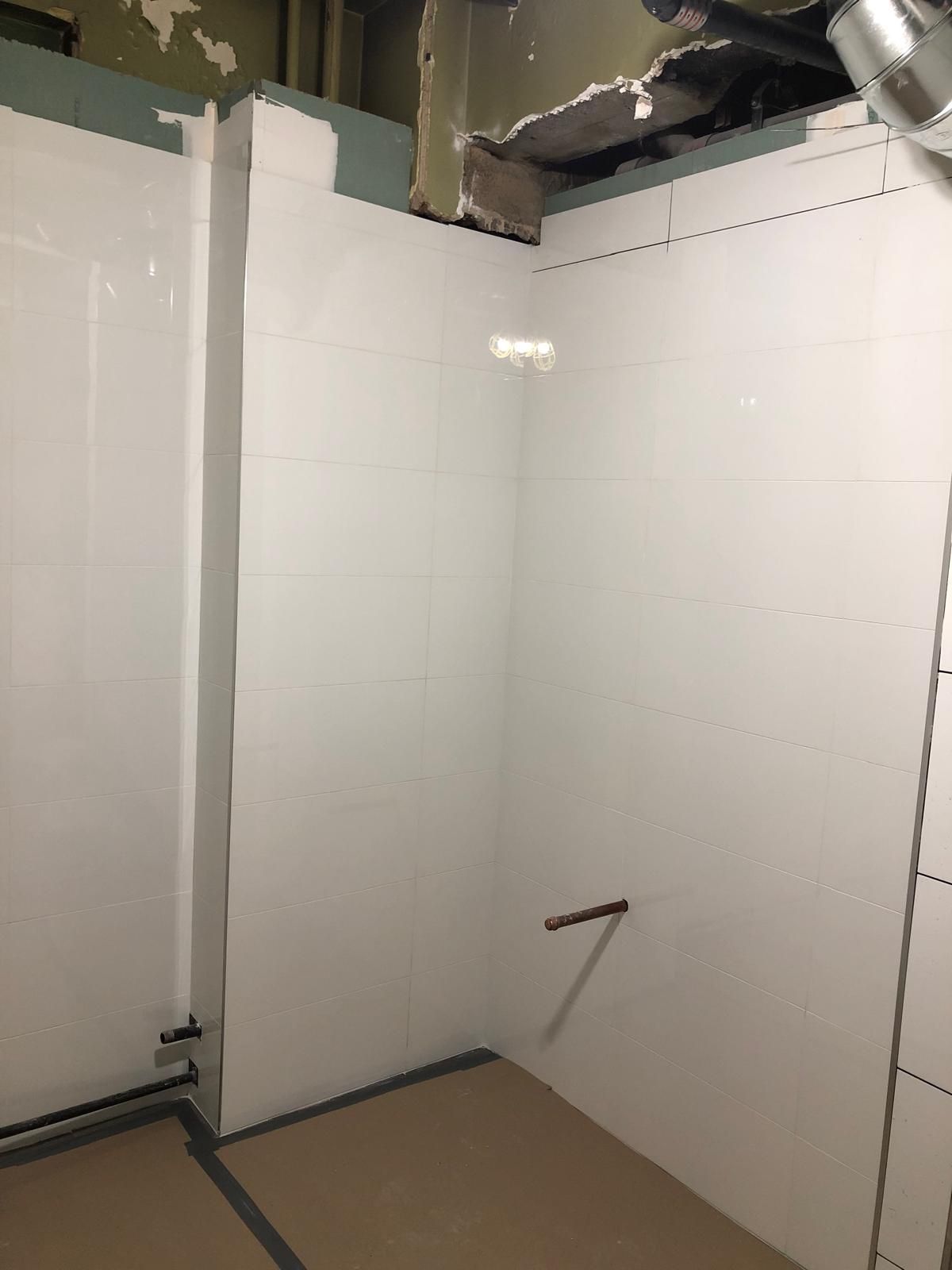 A bathroom with white tiles and a ladder in it