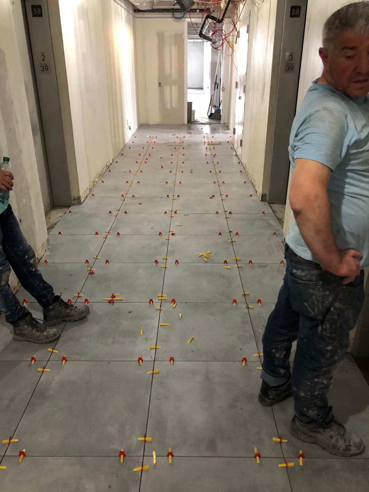 Two men are standing in a hallway with tiles on the floor.