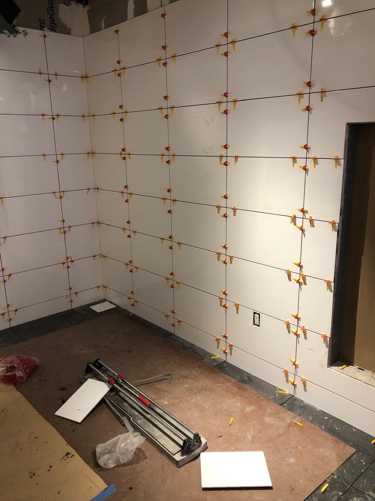 A room with a lot of tiles on the wall and a tile cutter on the floor.