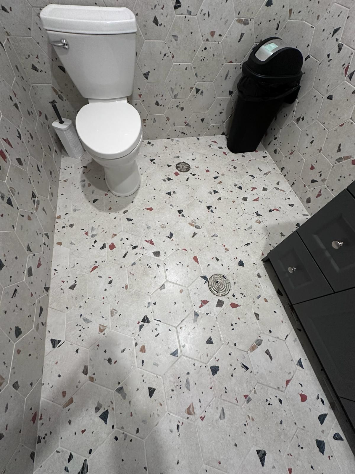 A bathroom with a toilet and a trash can on the floor.