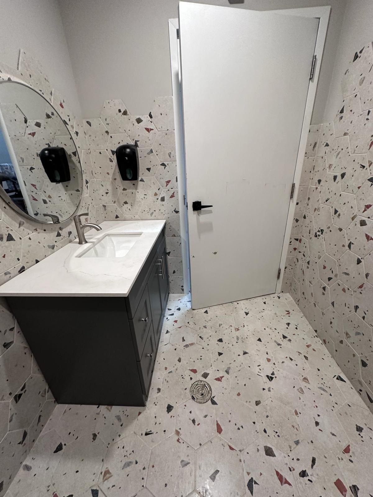 A bathroom with a sink , mirror , and terrazzo floor.