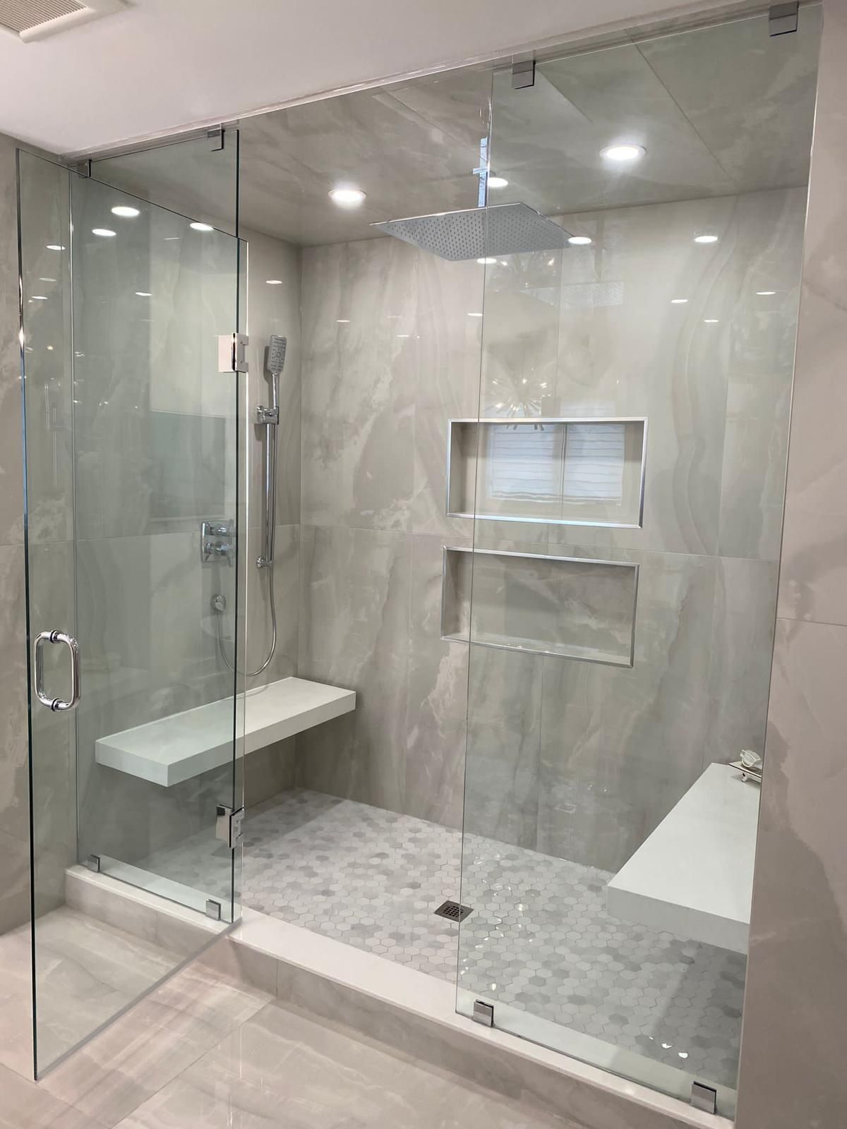 A bathroom with a walk in shower with a glass door and a bench.