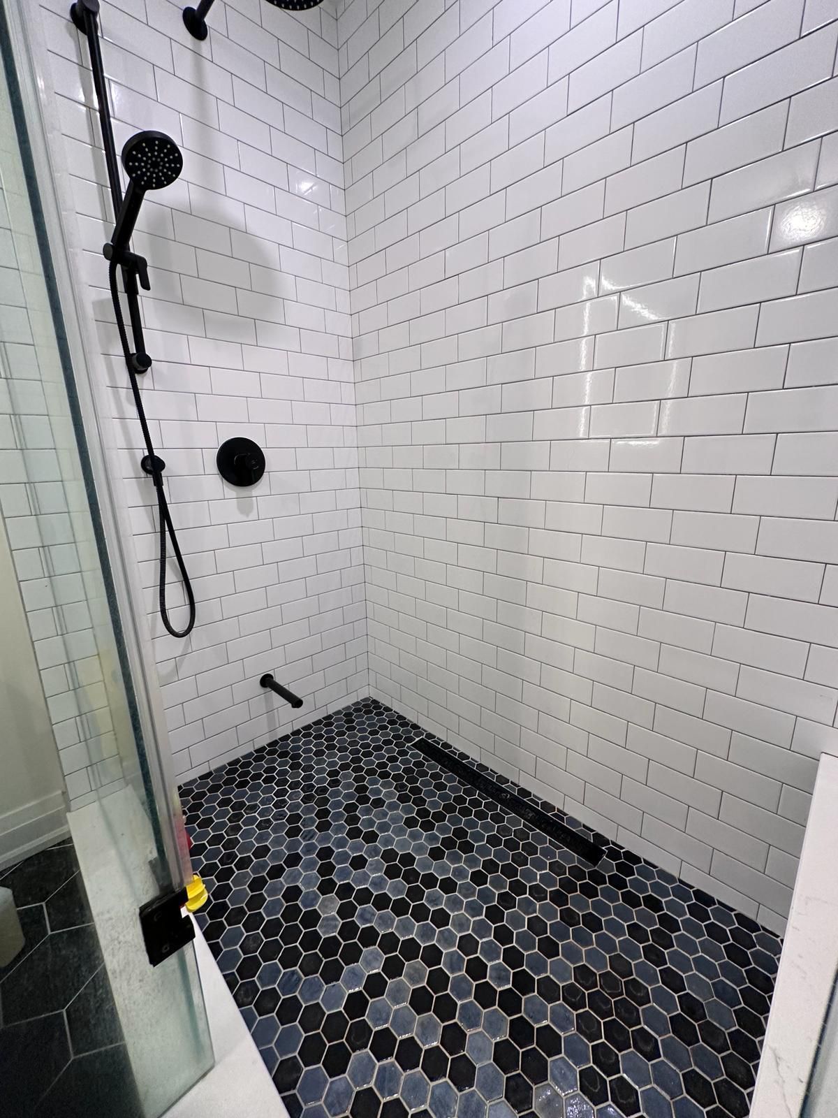 A shower with white brick walls and a black tile floor.