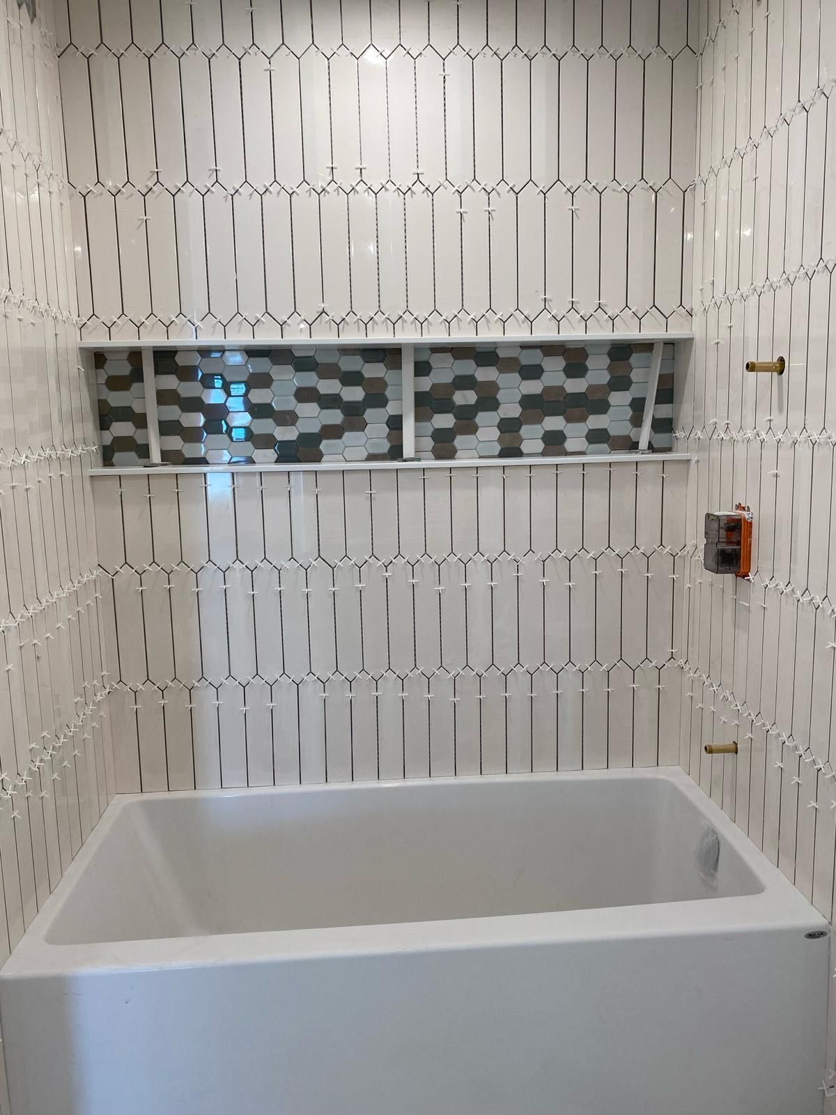 A bathtub in a bathroom with white tiles and a window.