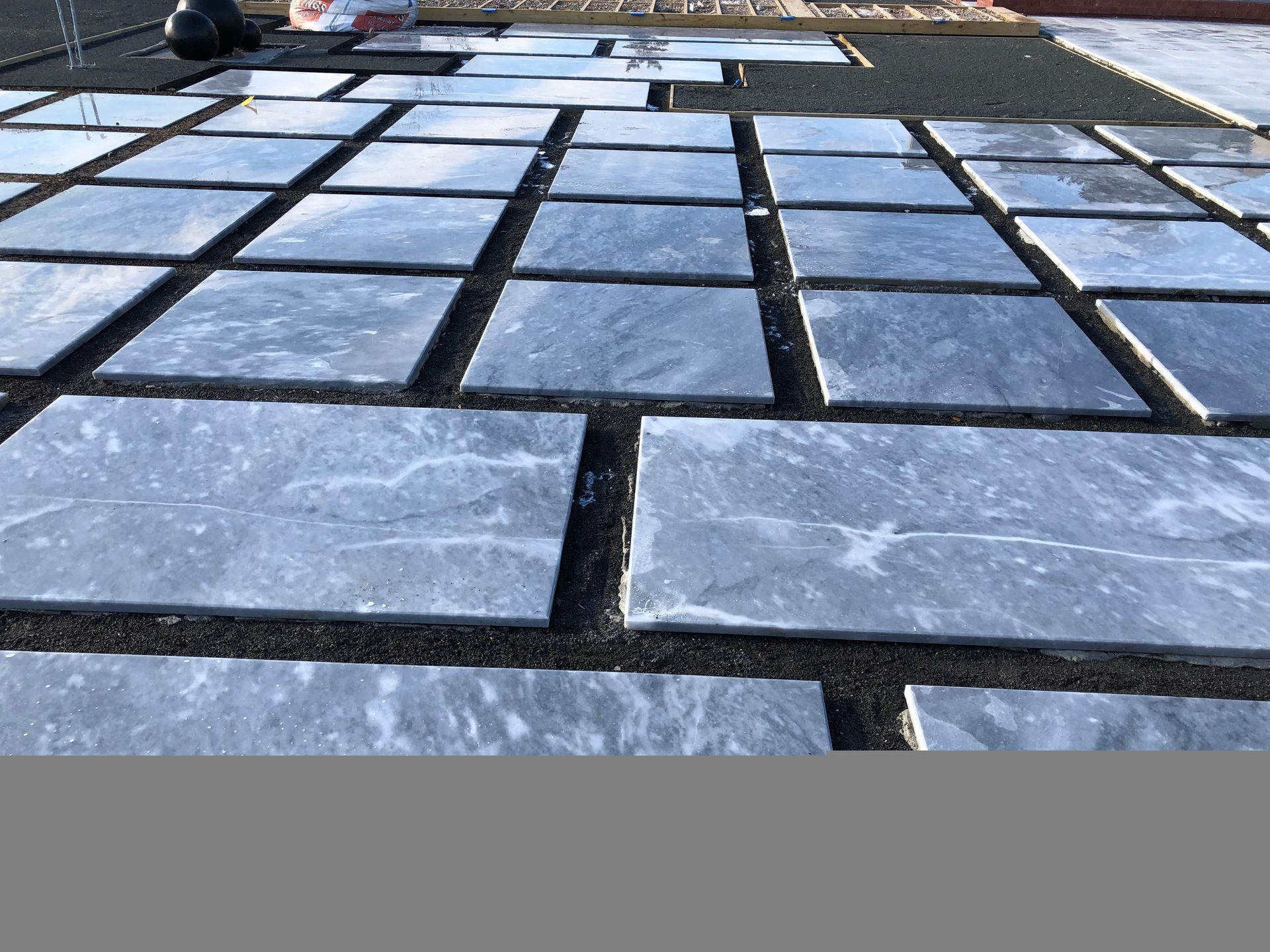 A person is laying tiles on a concrete surface.