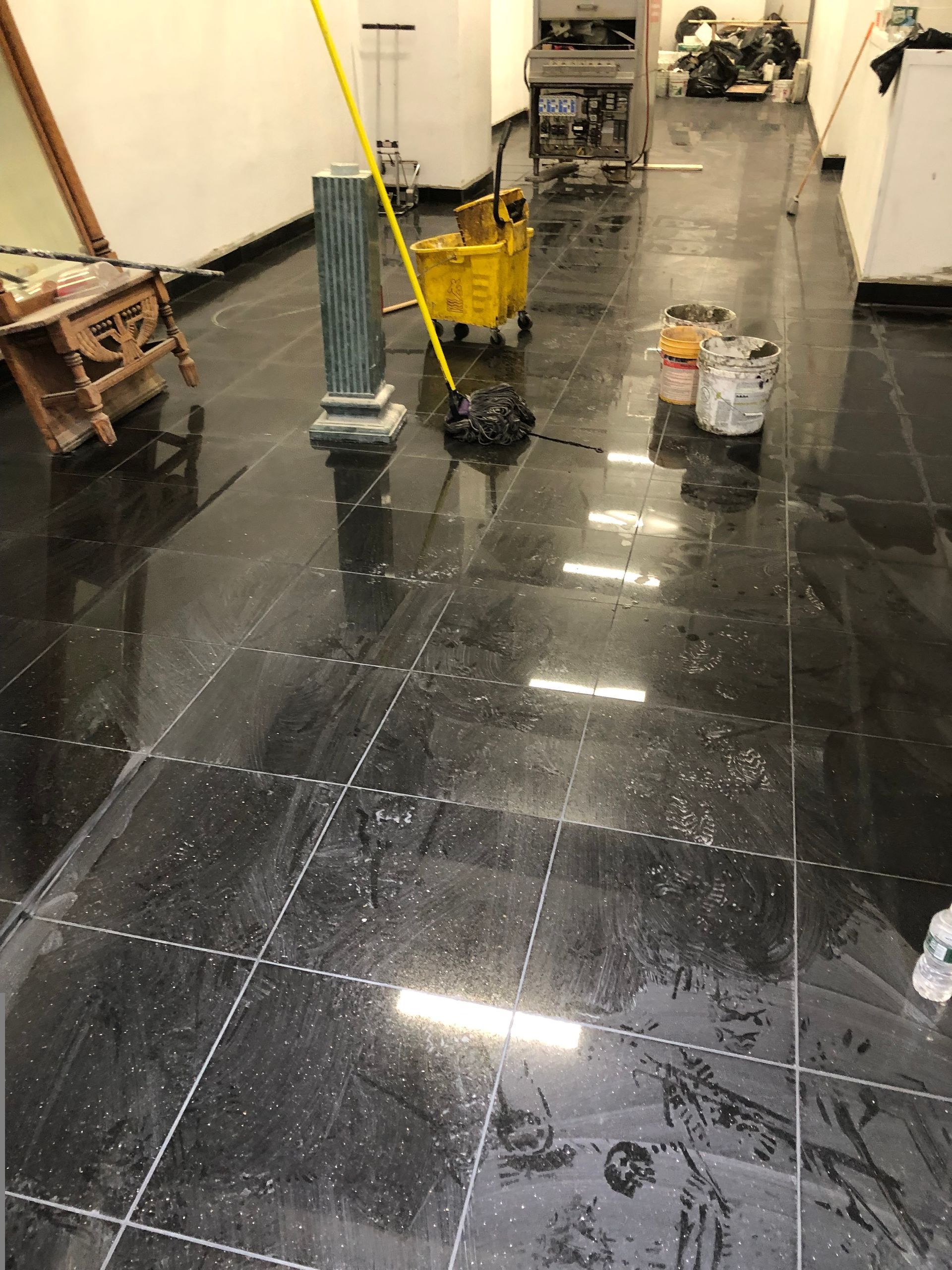 A black tiled floor with a yellow mop and buckets on it.