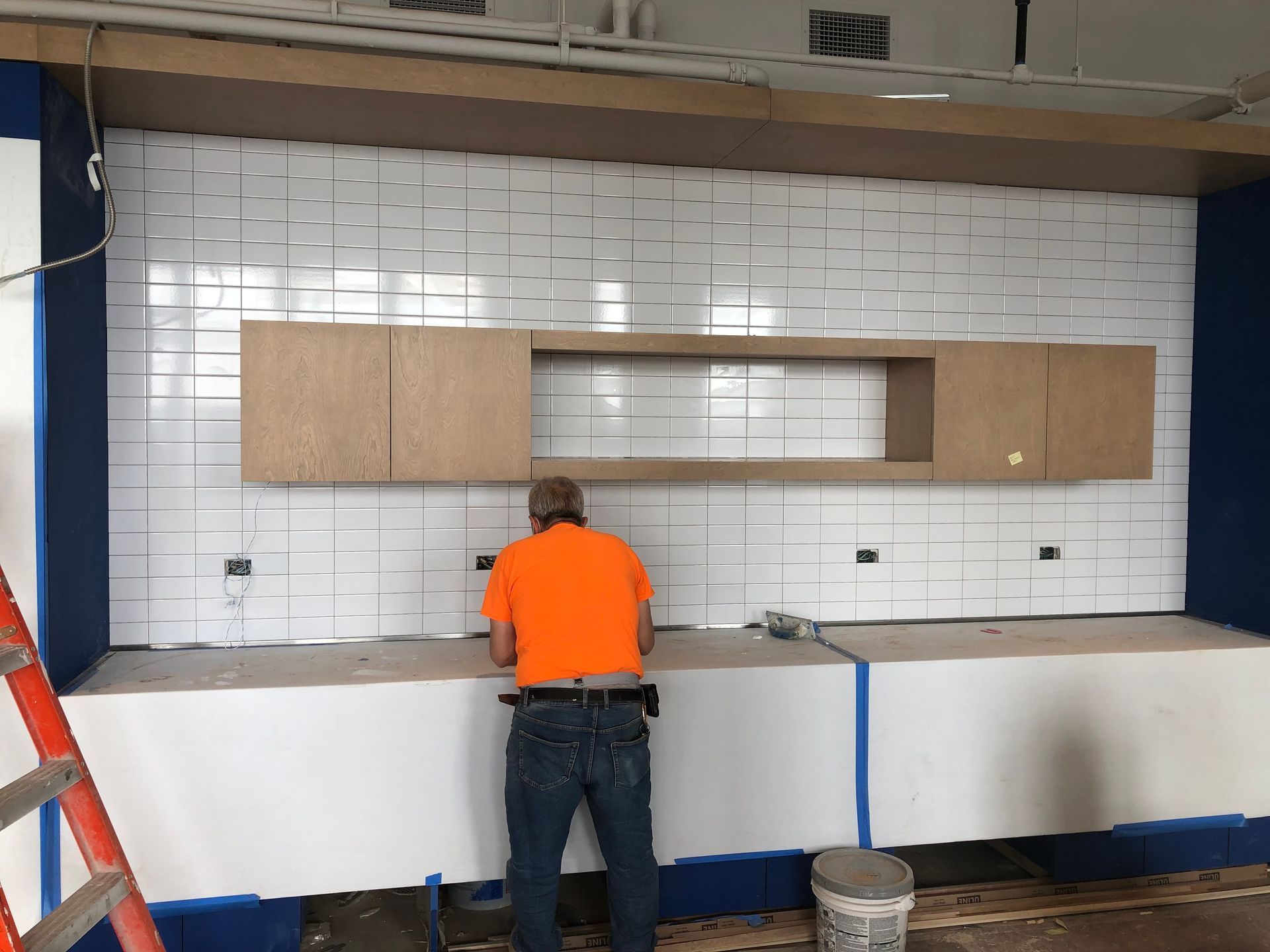 A man in an orange shirt is working on a kitchen counter.