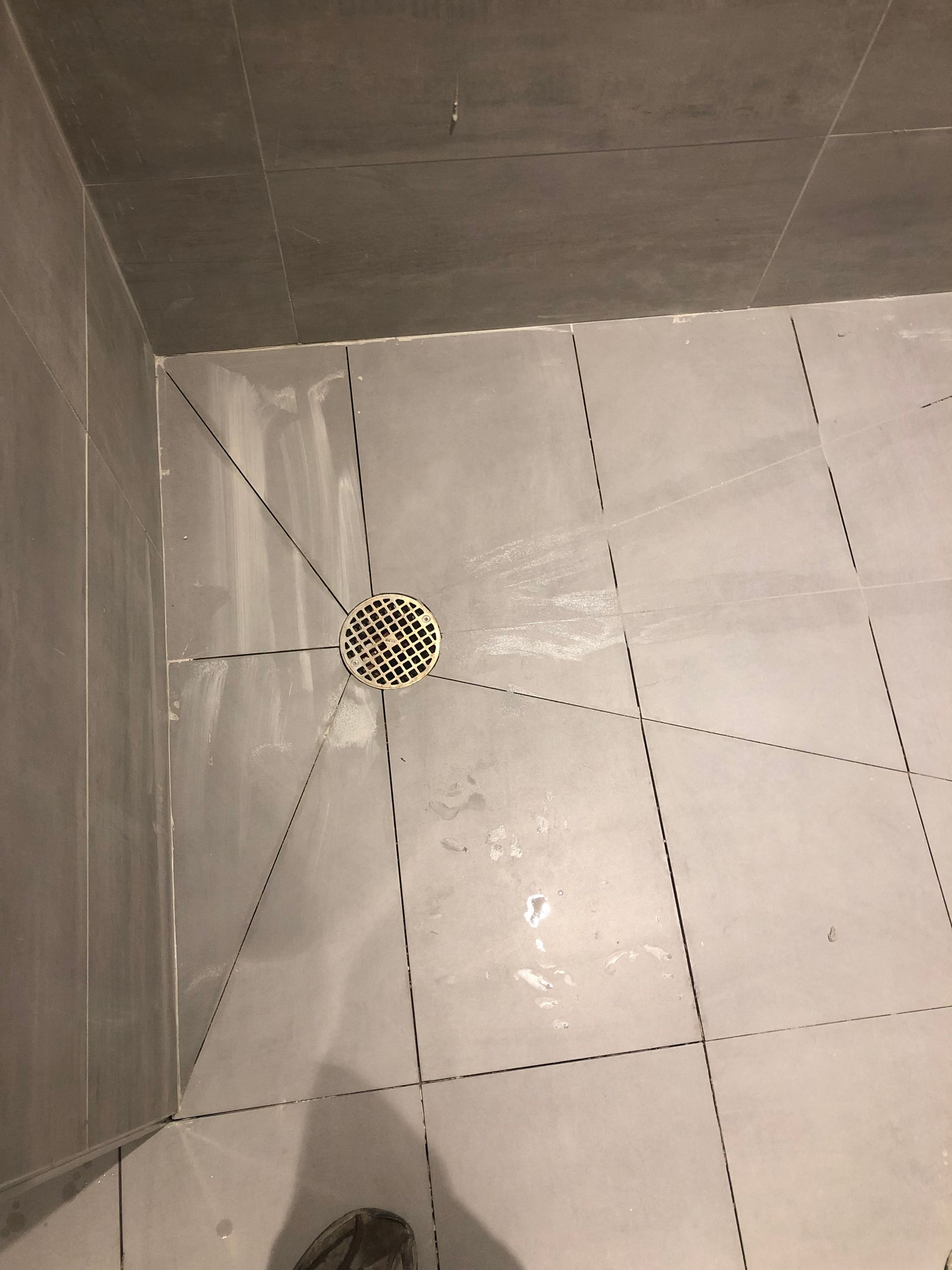 A person is standing in a bathroom with a drain on the floor.