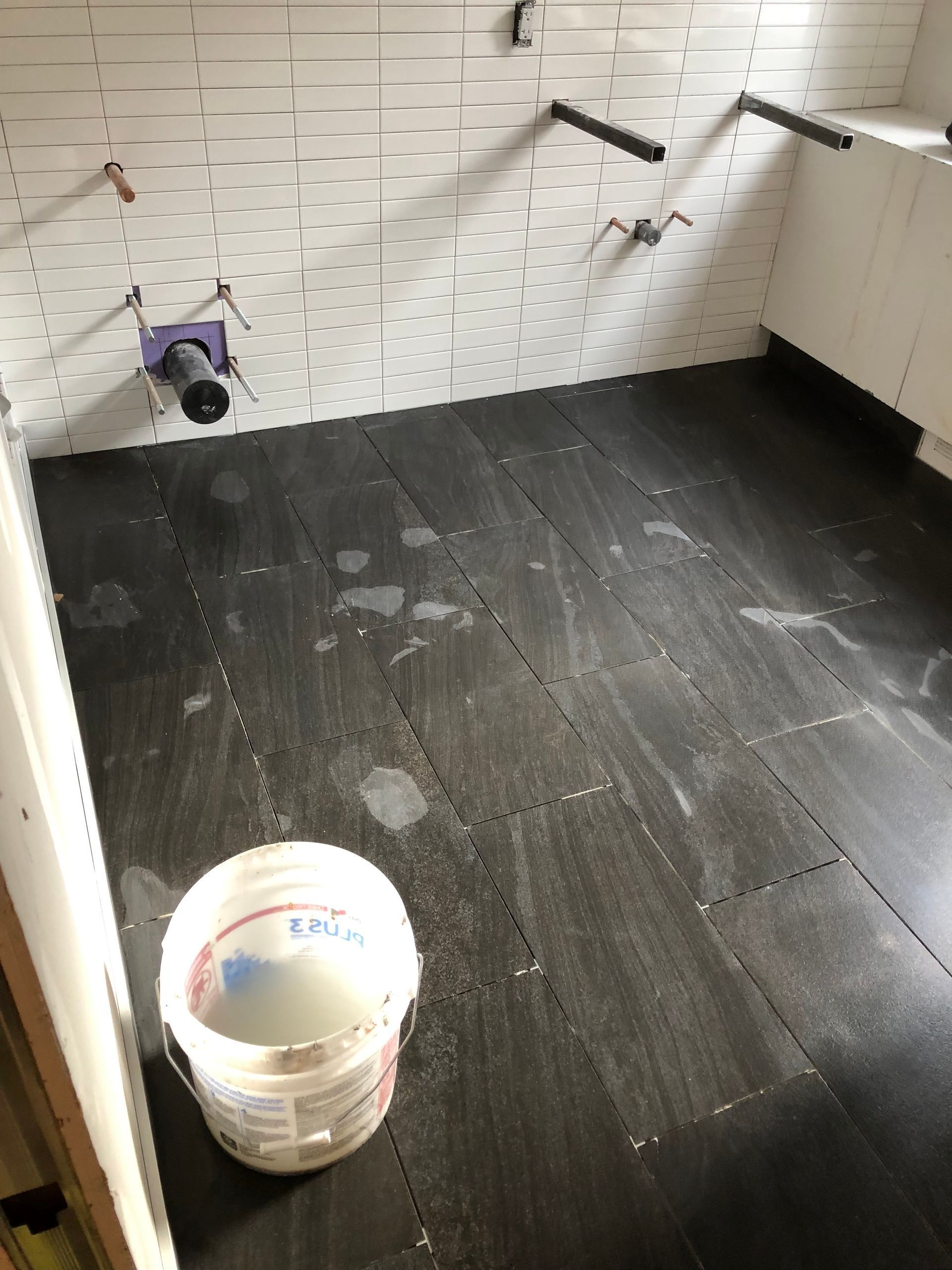 A bucket of water is sitting on the floor of a bathroom under construction.