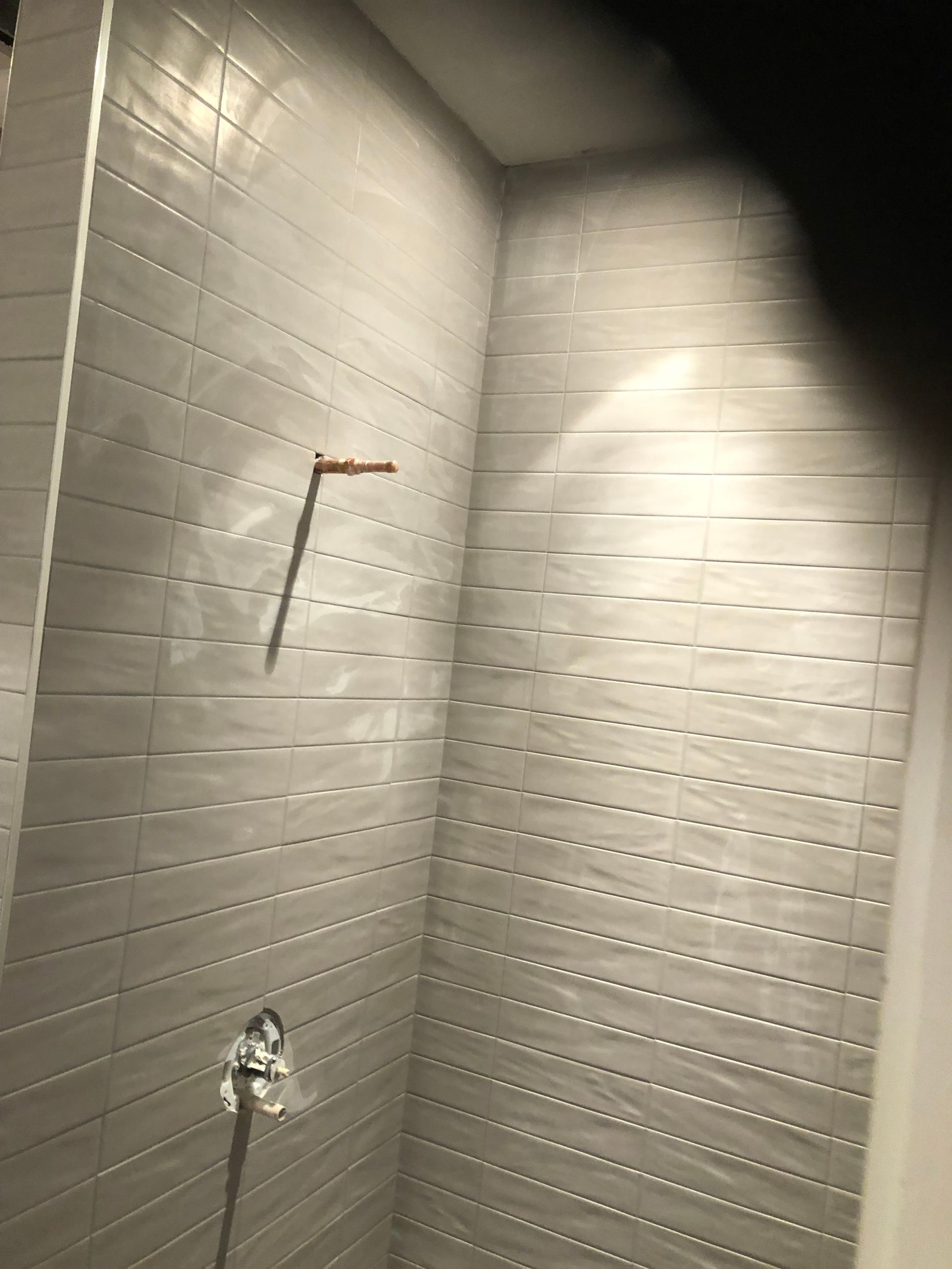 A bathroom with white tiles and a shower head.