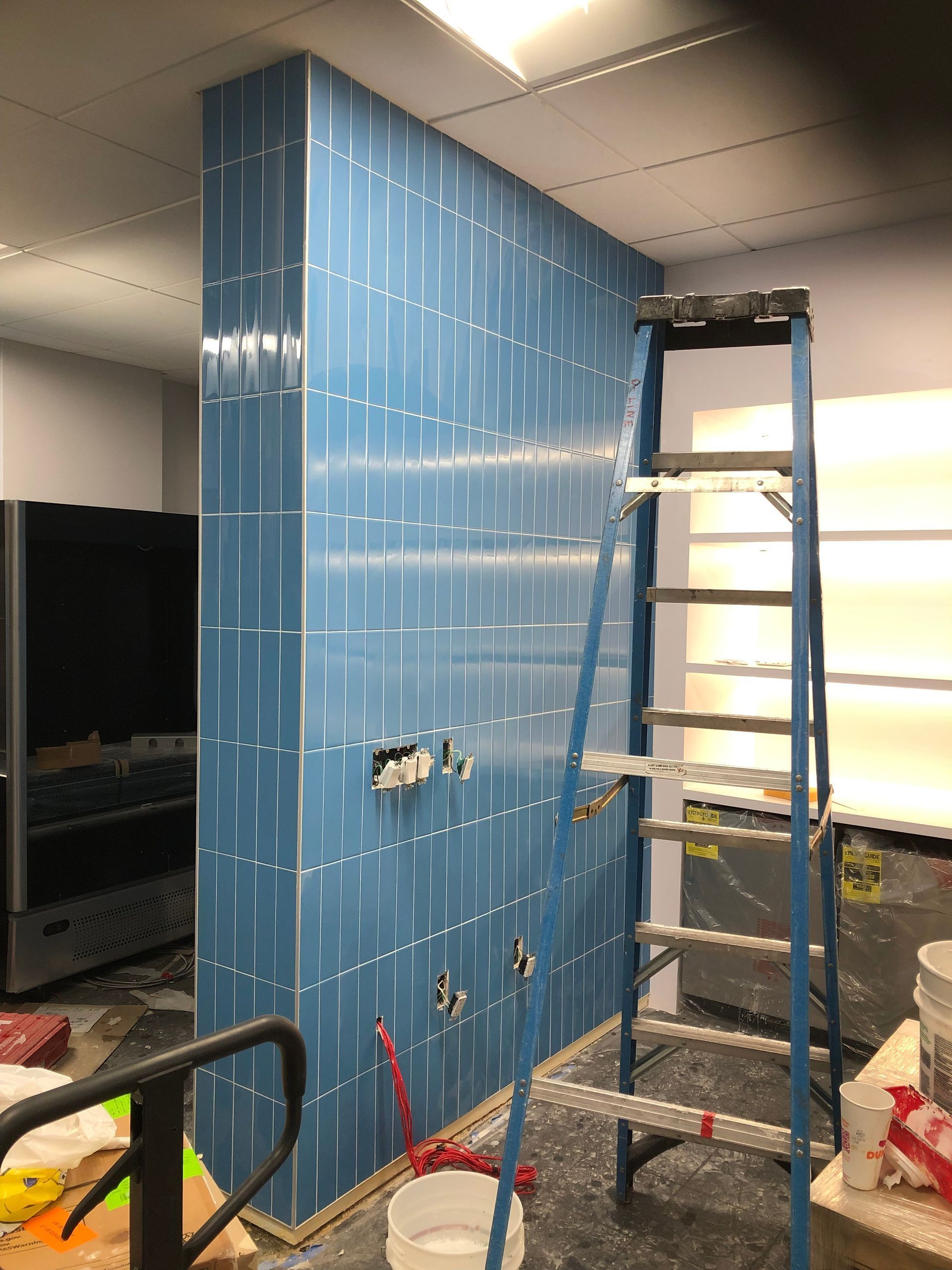 A ladder is sitting in front of a blue tiled wall.