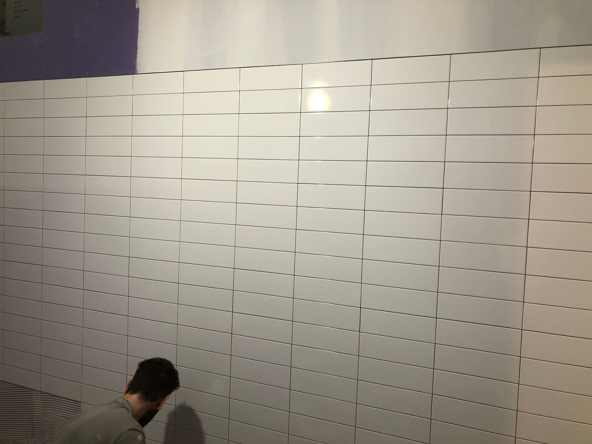 A man is standing in front of a wall of white tiles