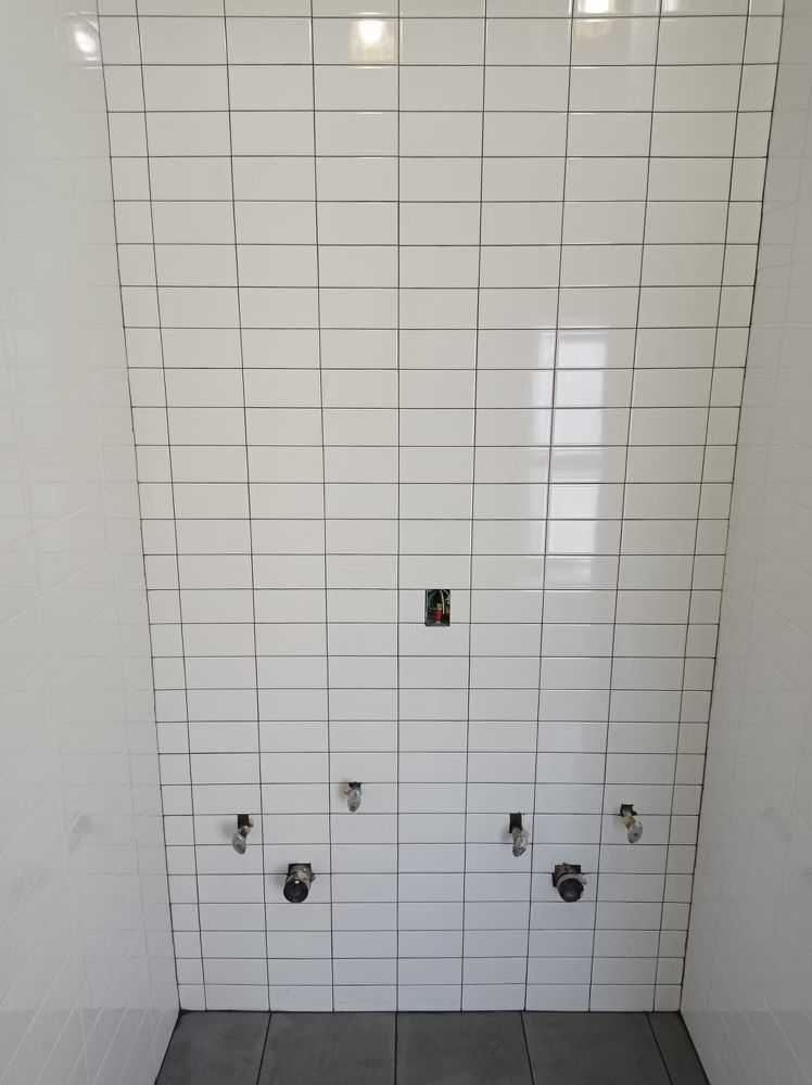 A bathroom with white tiles and faucets on the wall