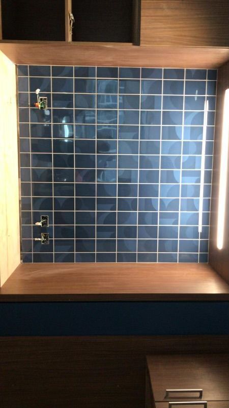 A wall with blue tiles and a wooden shelf underneath it.