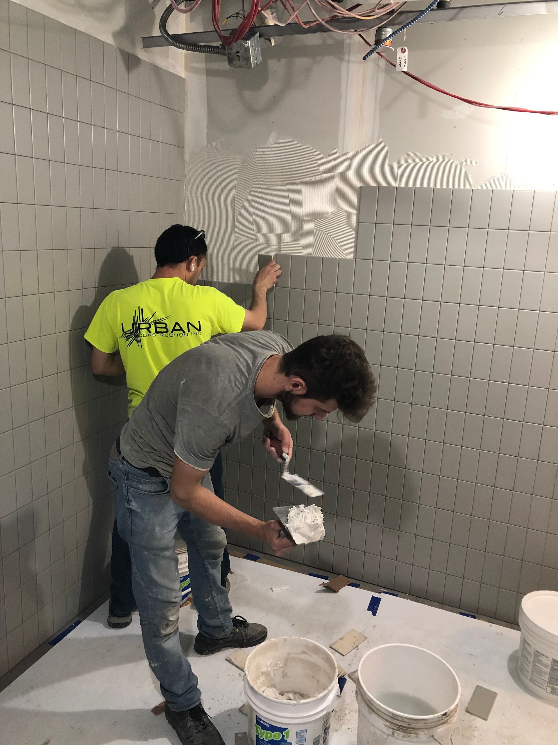 Two men are working on a wall in a room.