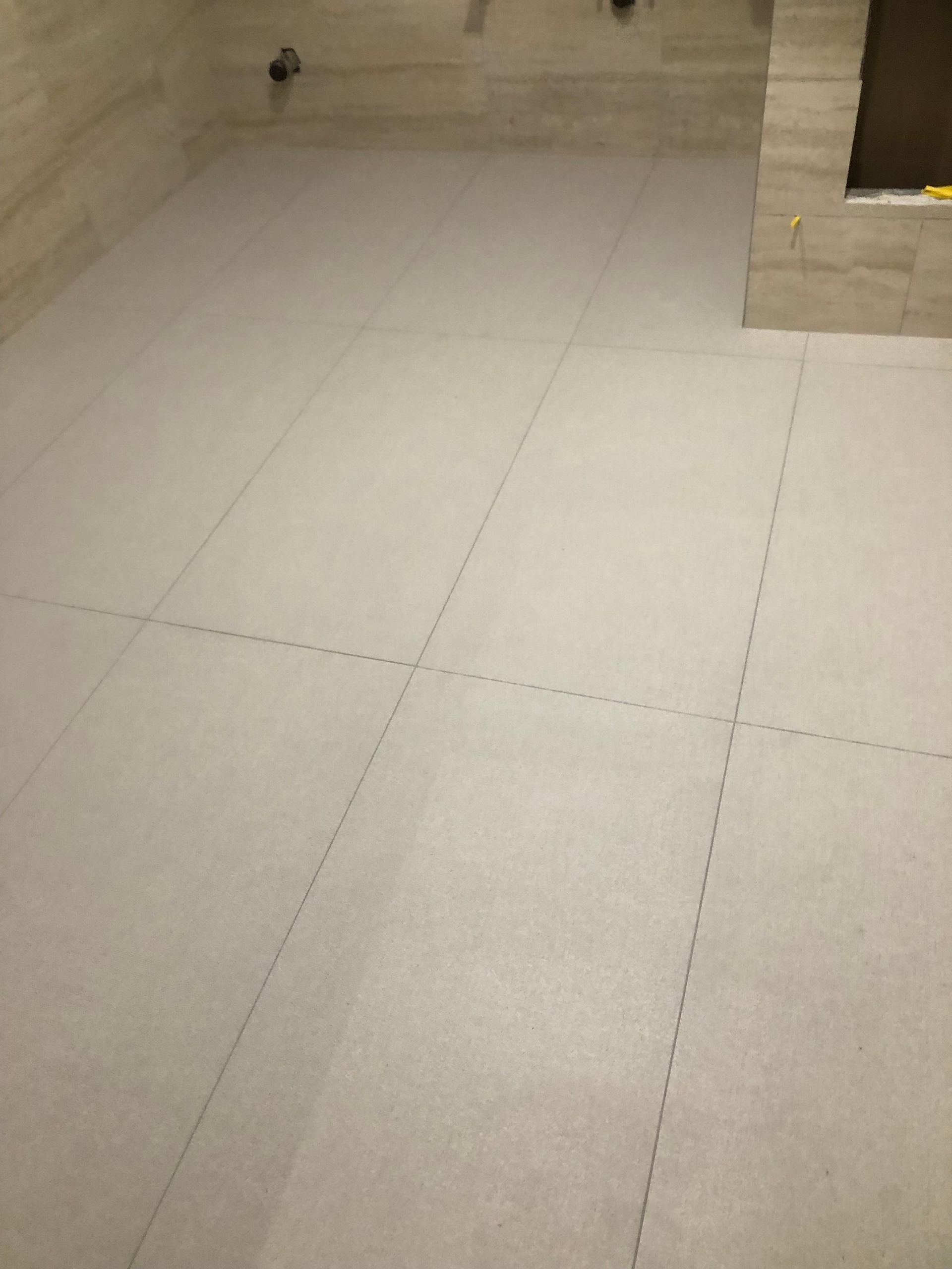 A large white tile floor in a room with a marble wall.