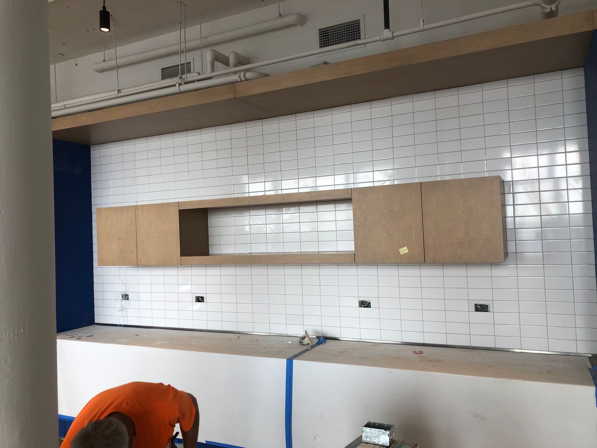 A man is kneeling down in front of a wall with white tiles.