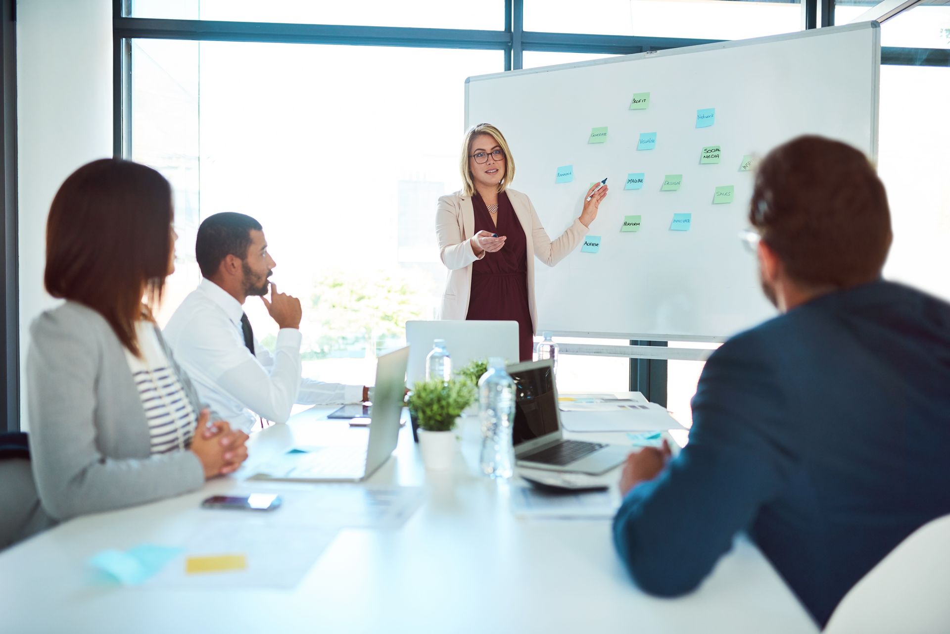 Businesswoman presenting ideas on a whiteboard to colleagues in a modern office.