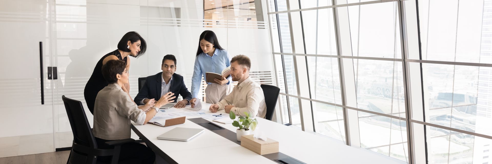 Business colleagues in a meeting at a conference table with a large window in the background.