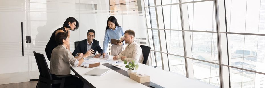 Business colleagues in a meeting at a conference table with a large window in the background.