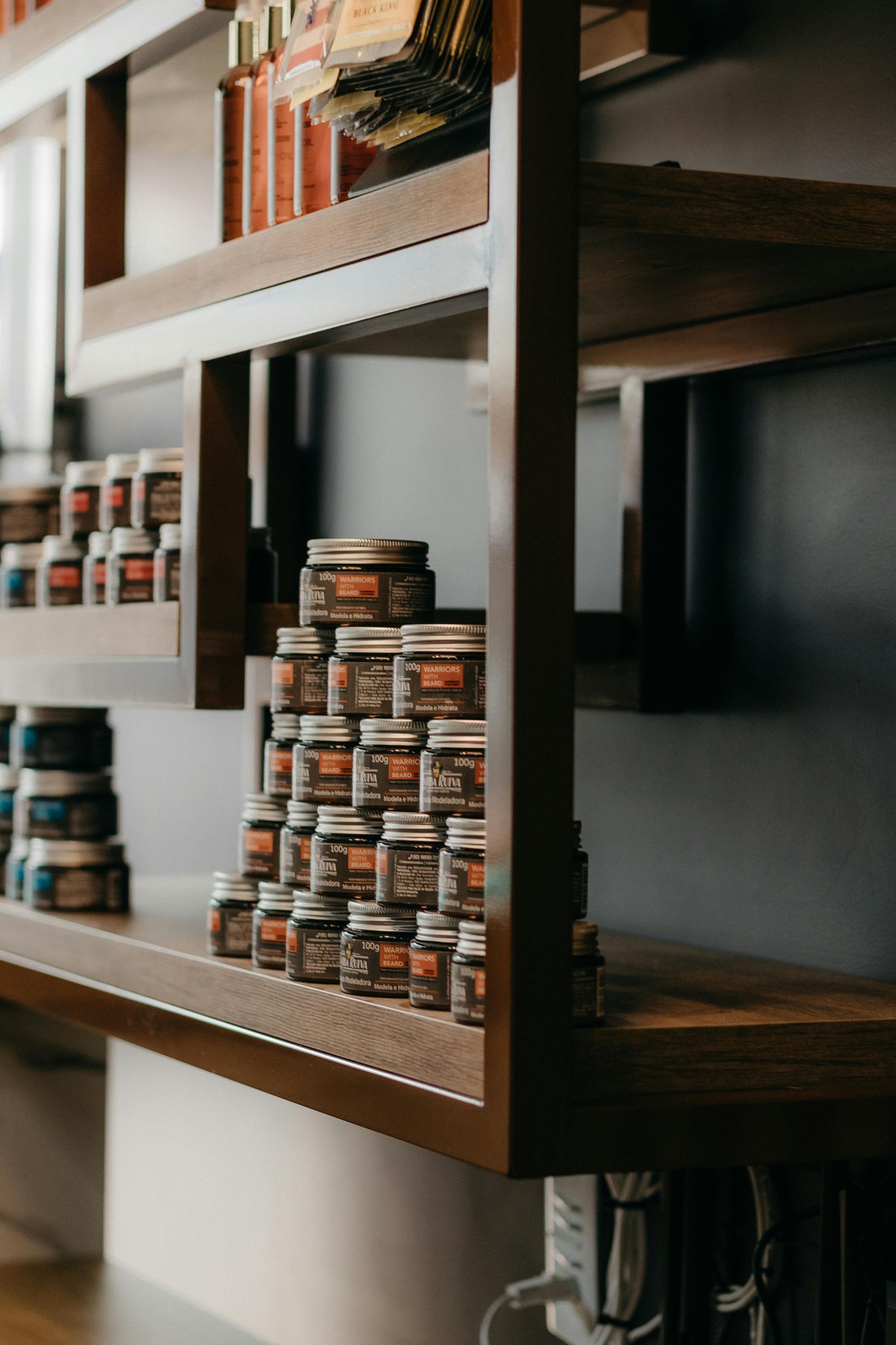Shelves stacked with jars of various sizes and labels. Dark wood framing, gray wall background.