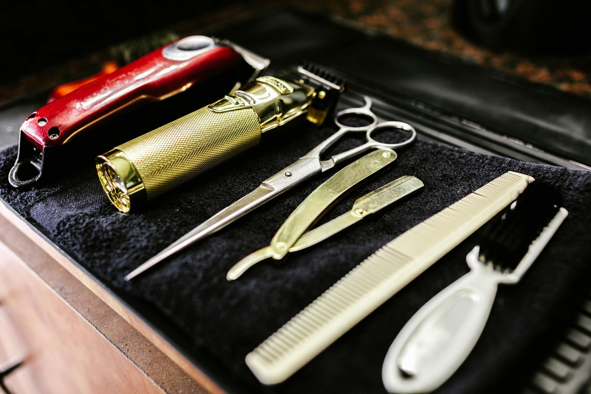 Barber tools: clippers, scissors, razor, comb, and brush on a dark cloth.