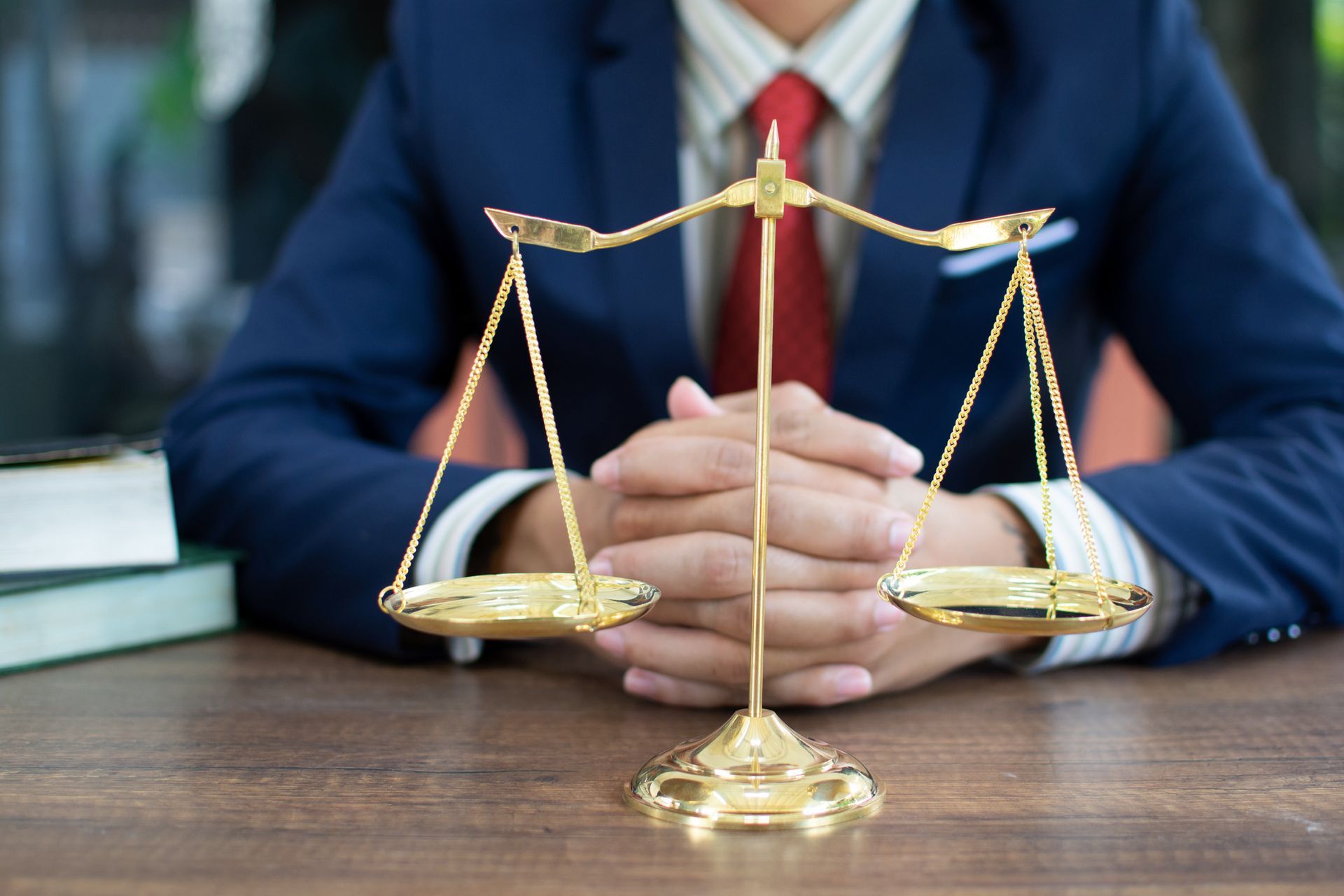 Personal injury attorney in suit behind justice scales at desk in legal office setting.