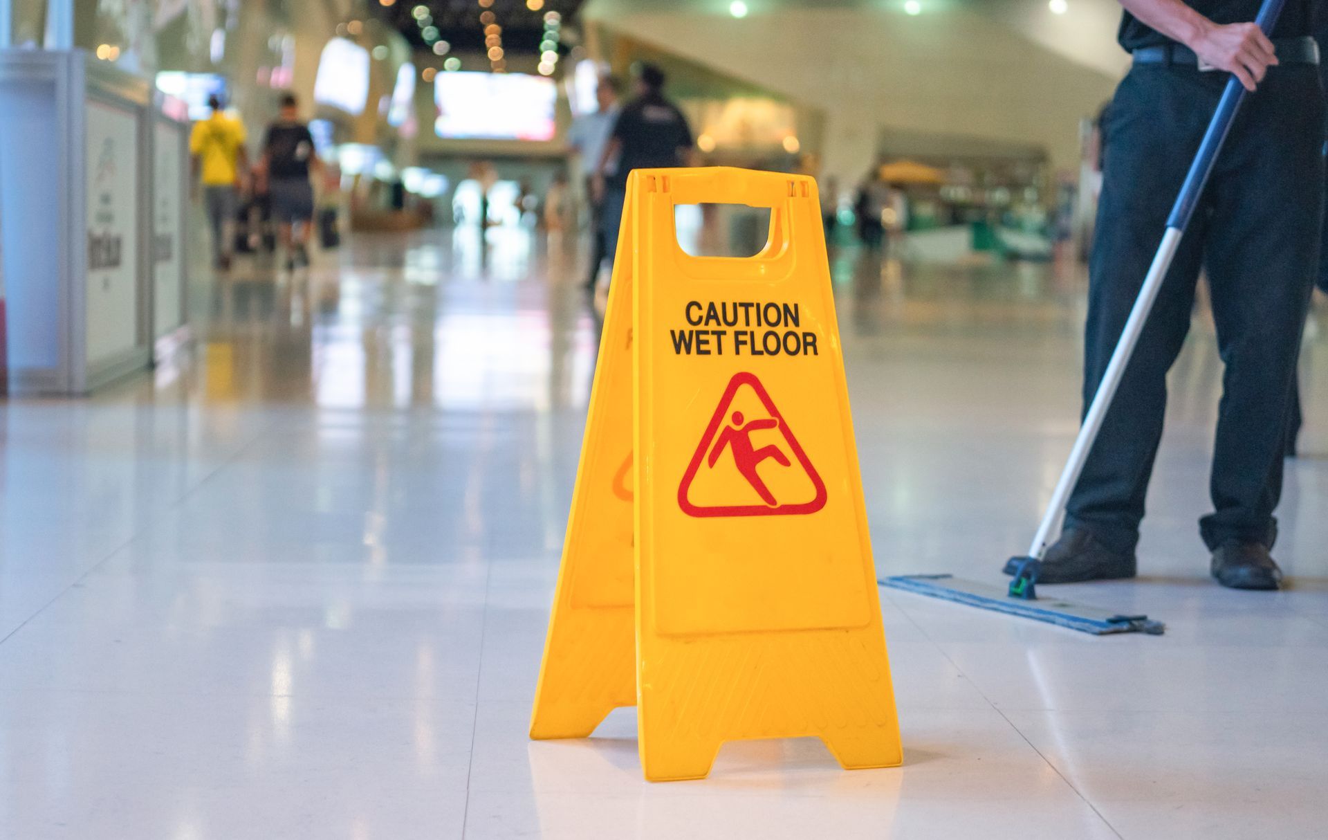 A man is mopping the floor next to a caution wet floor sign – Saint Joseph, MO – Eslinger Law Firm