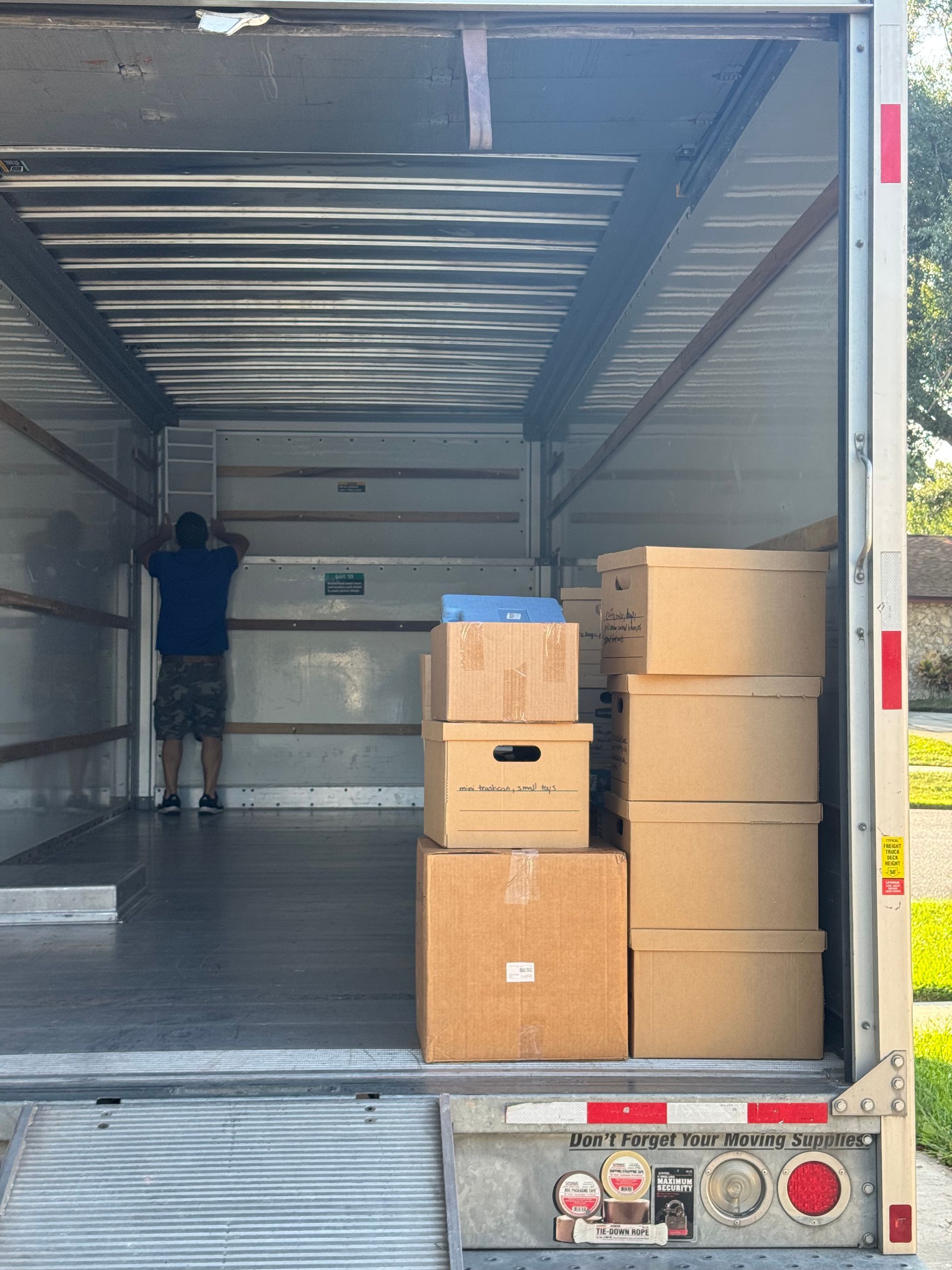 Man standing inside a moving truck loading boxes. Boxes stacked on the right, ramp down.