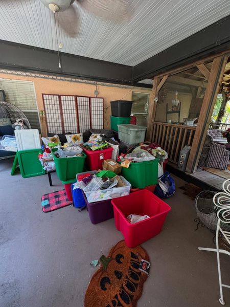 A cluttered outdoor porch with storage bins, rugs, and various items scattered about.