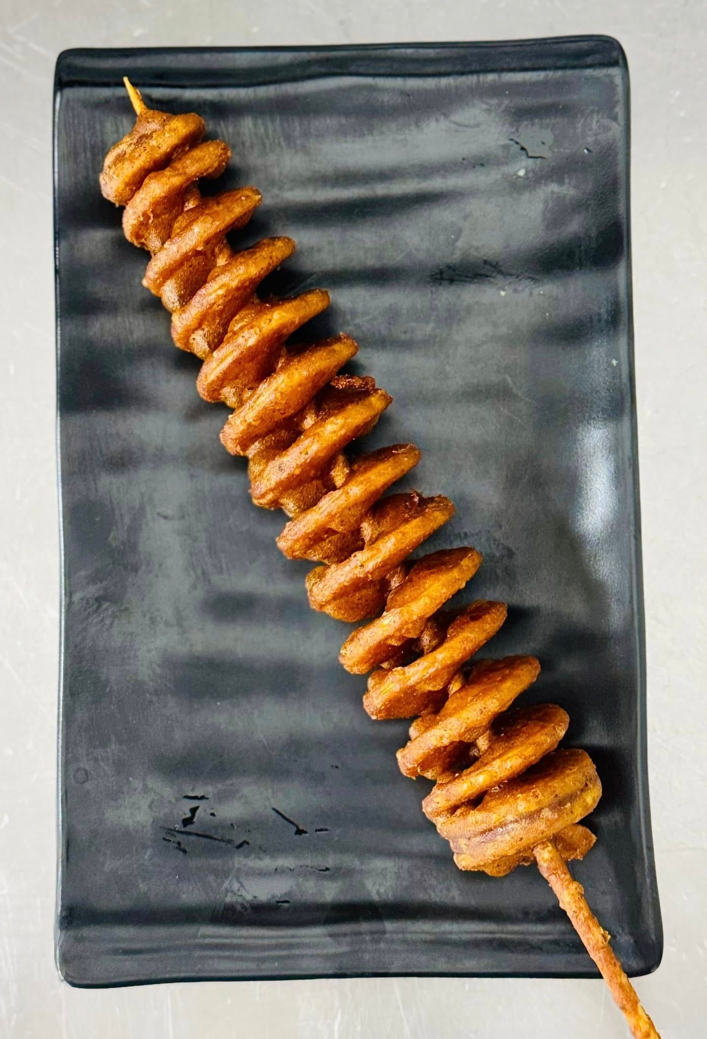 Spiral-cut Potato on a Skewer, Fried and Served on a Dark Rectangular Plate — Pt Cartwright Seafoods in Warana, QLD