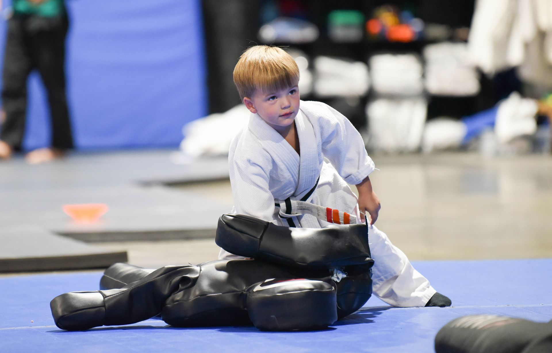 A young boy in a karate uniform is sitting on top of a mannequin.