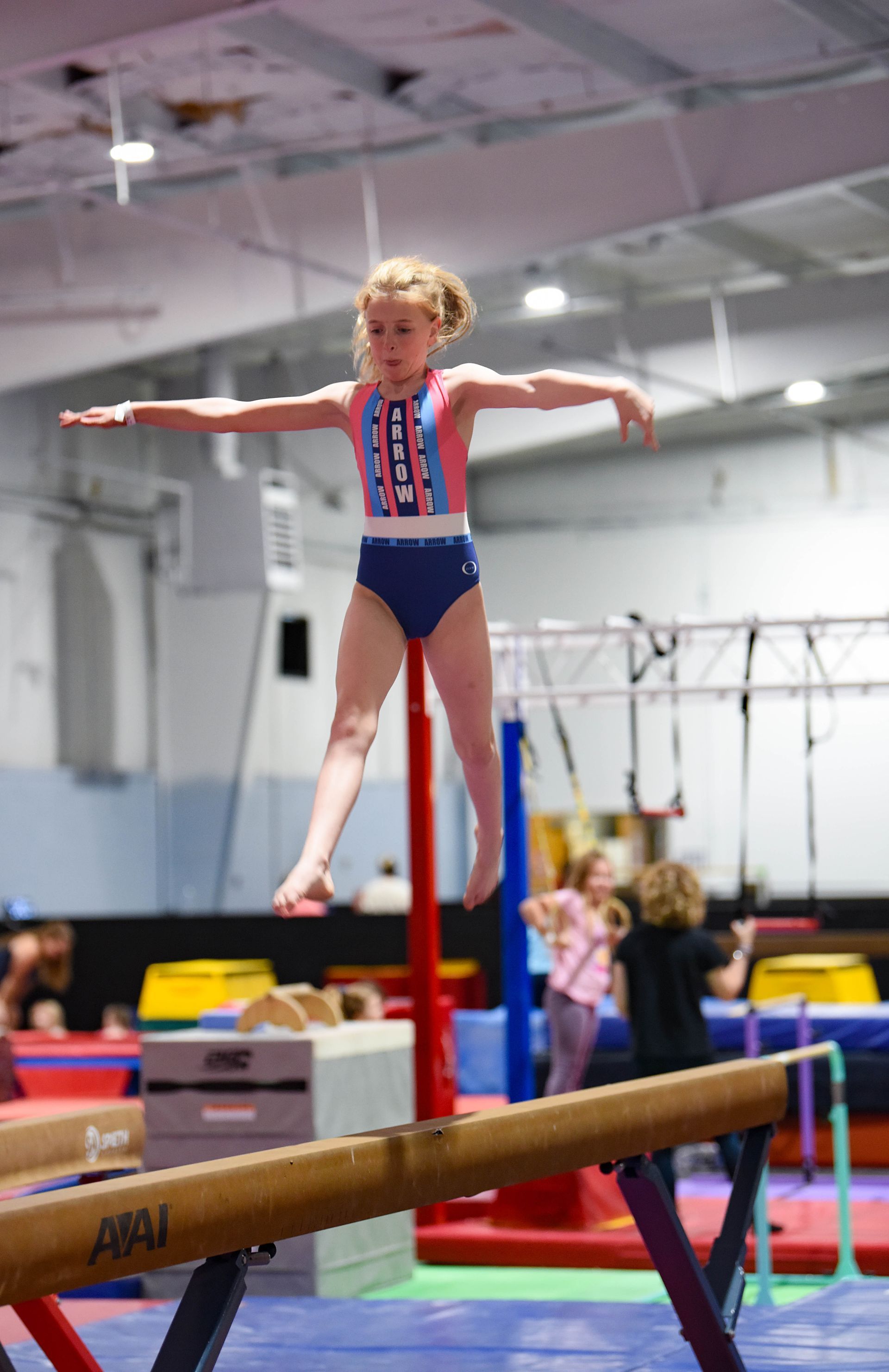 A young girl is standing on a balance beam in a gym.