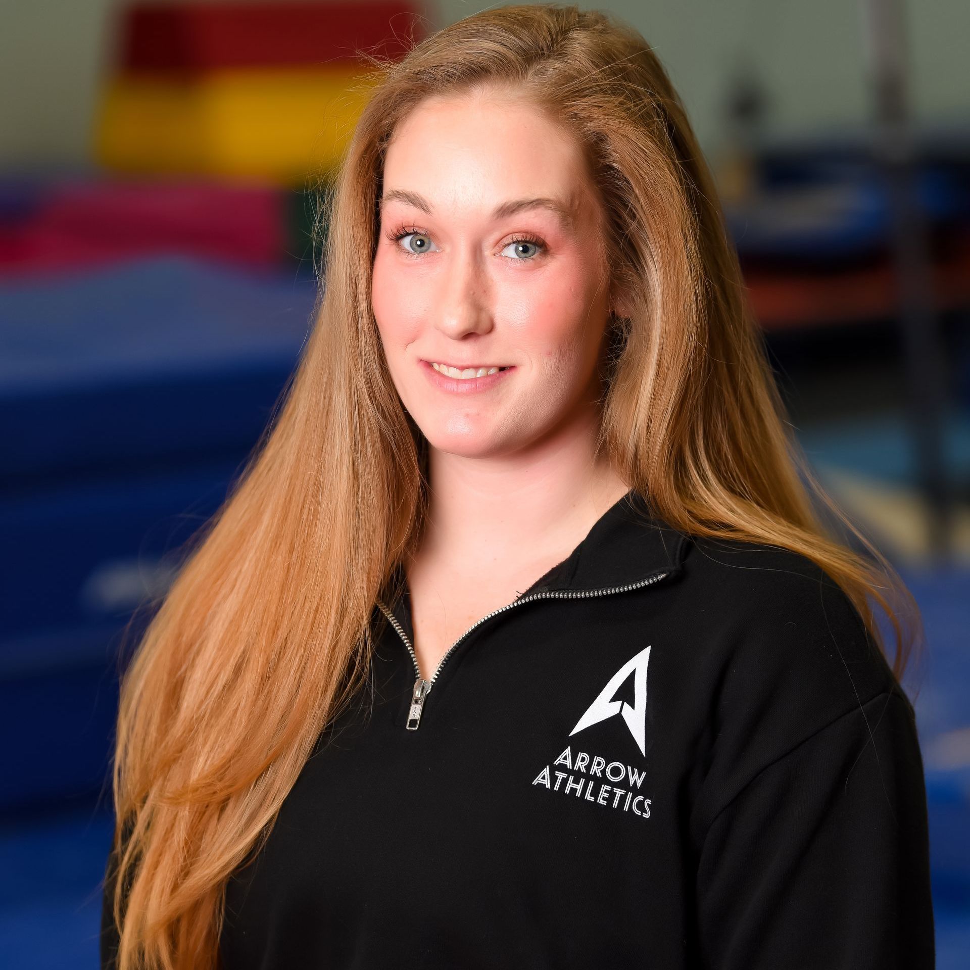 A woman wearing a black arrow athletics sweatshirt is smiling for the camera.