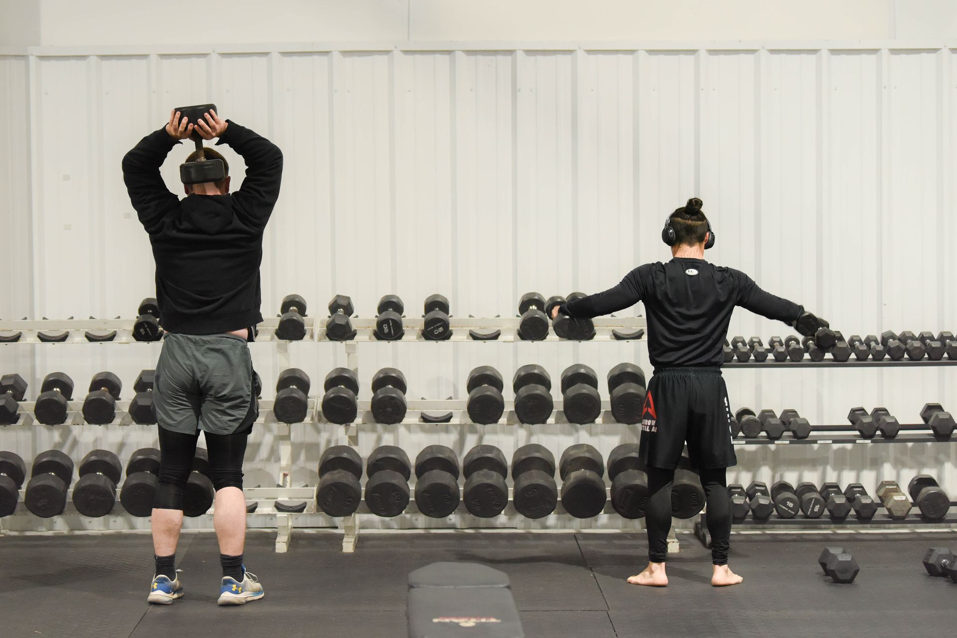 A man and a woman are standing in front of a rack of dumbbells in a gym.