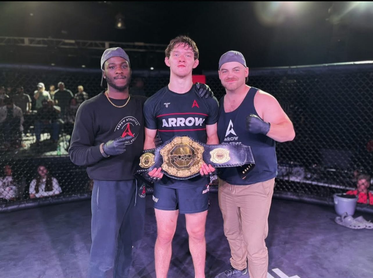 A man in an arrow shirt is standing with two other men