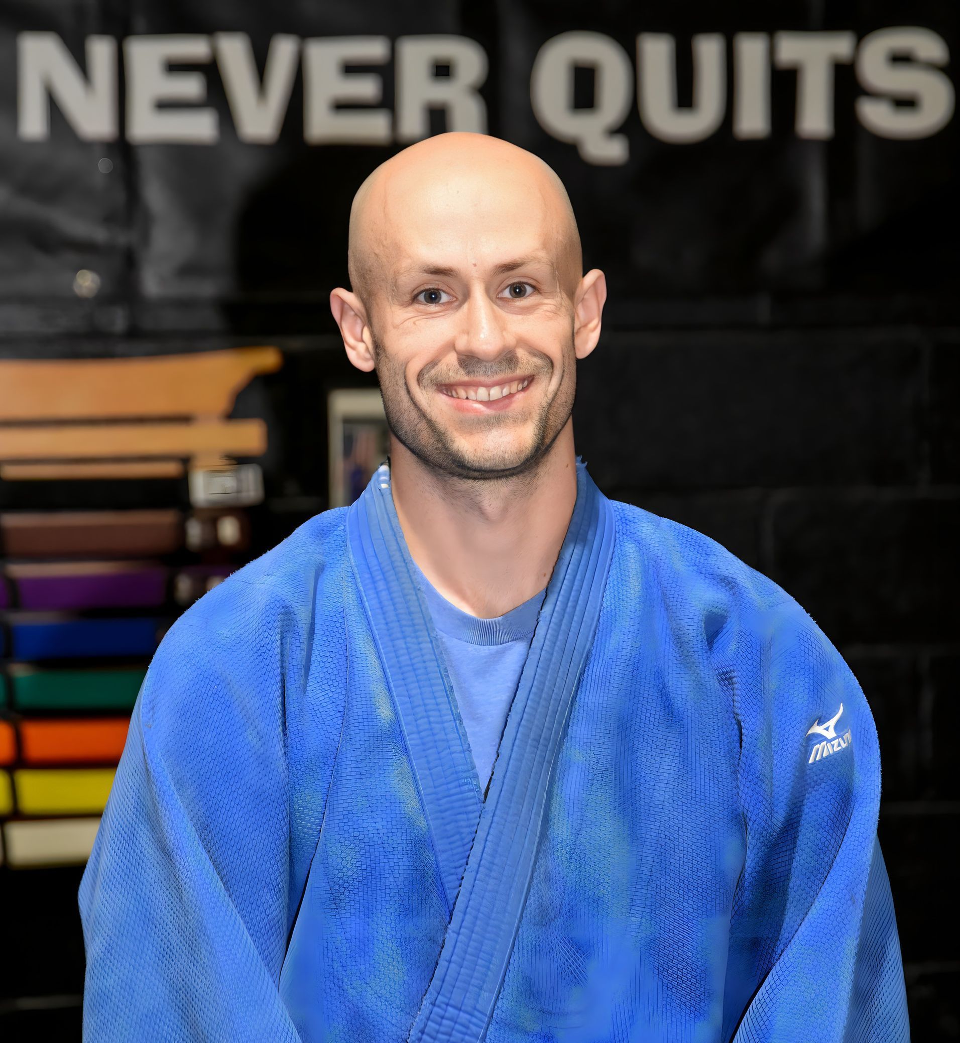 A man in a blue kimono is smiling in front of a sign that says never quits