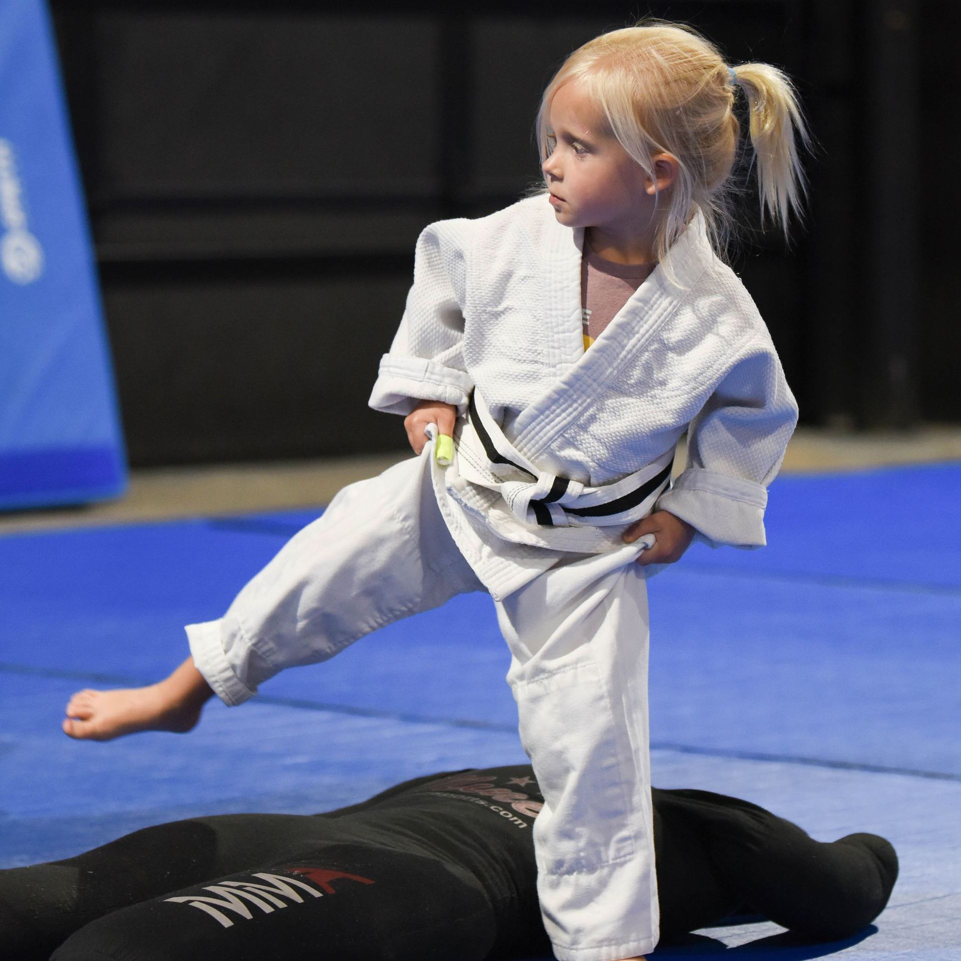 A little girl in a karate uniform is standing on a mat