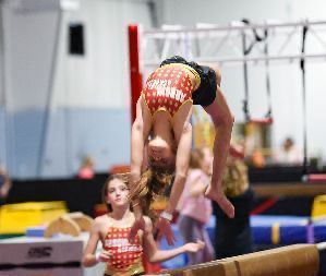 A young girl is doing a handstand on a balance beam in a gym.