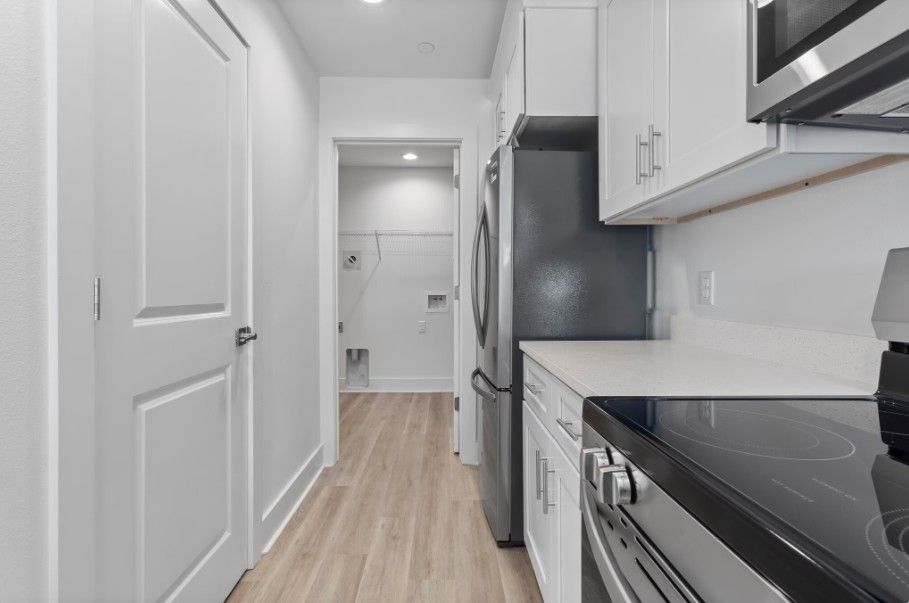 apartment kitchen and laundry room in Biloxi with stainless steel appliances, white cabinets, quartz countertops and wood floors