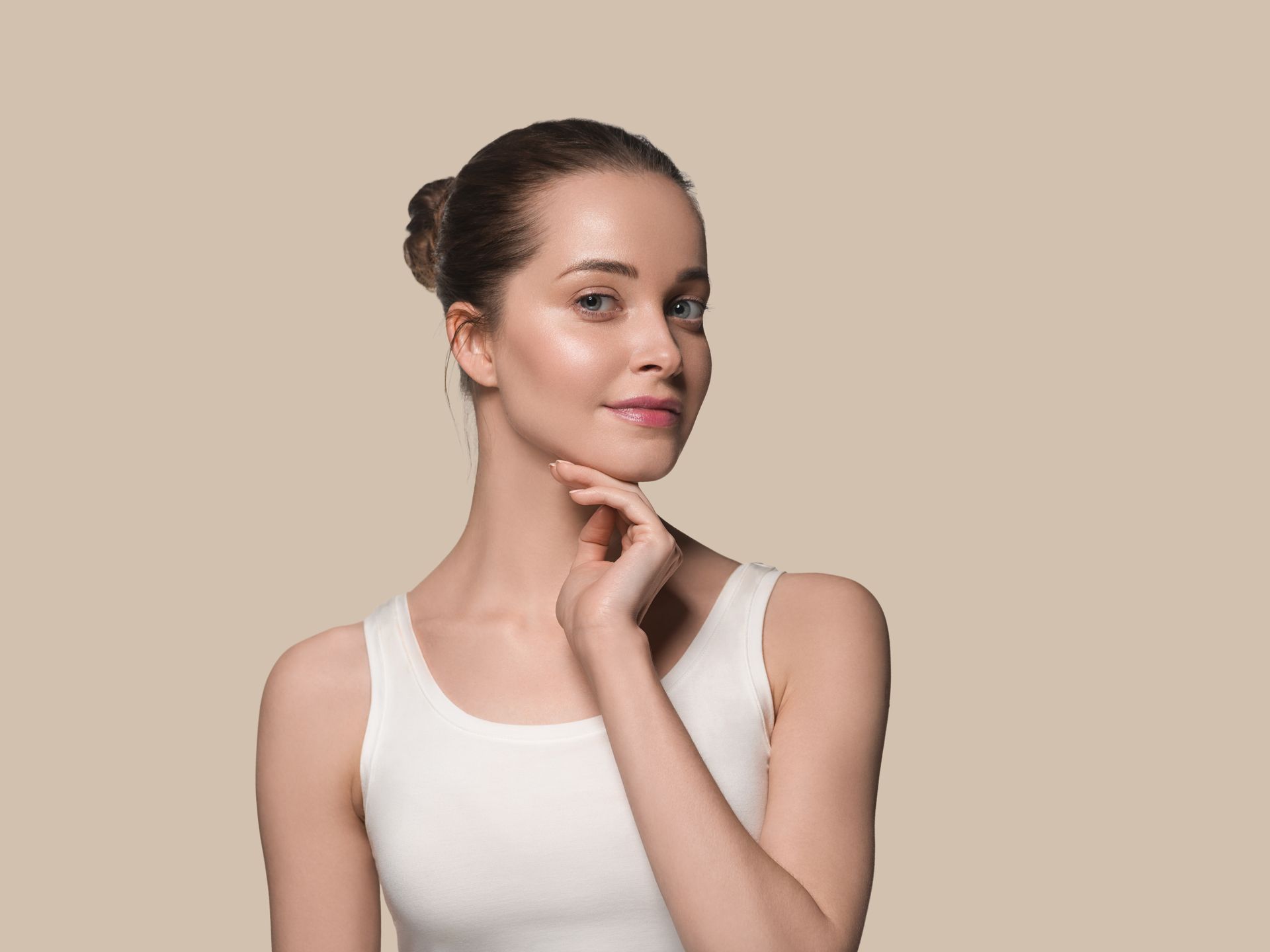 A woman in a white tank top is touching her face and smiling.