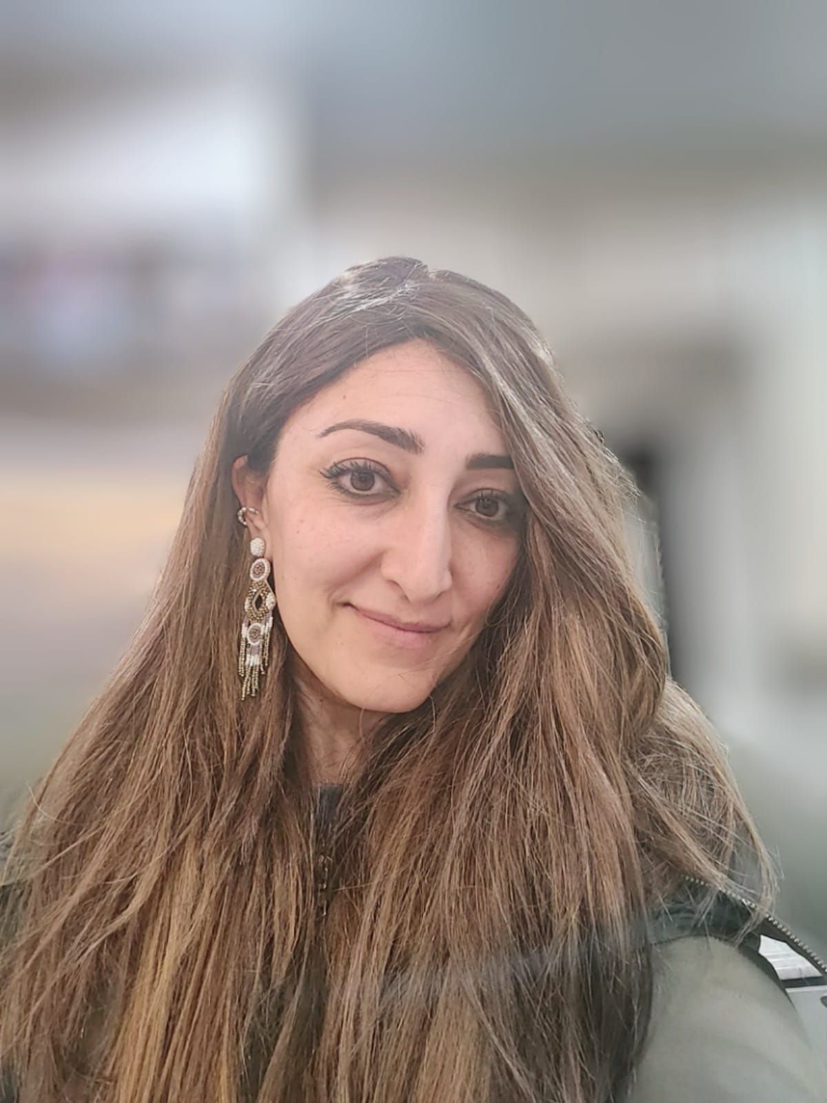 A woman with long brown hair and earrings is smiling for the camera.