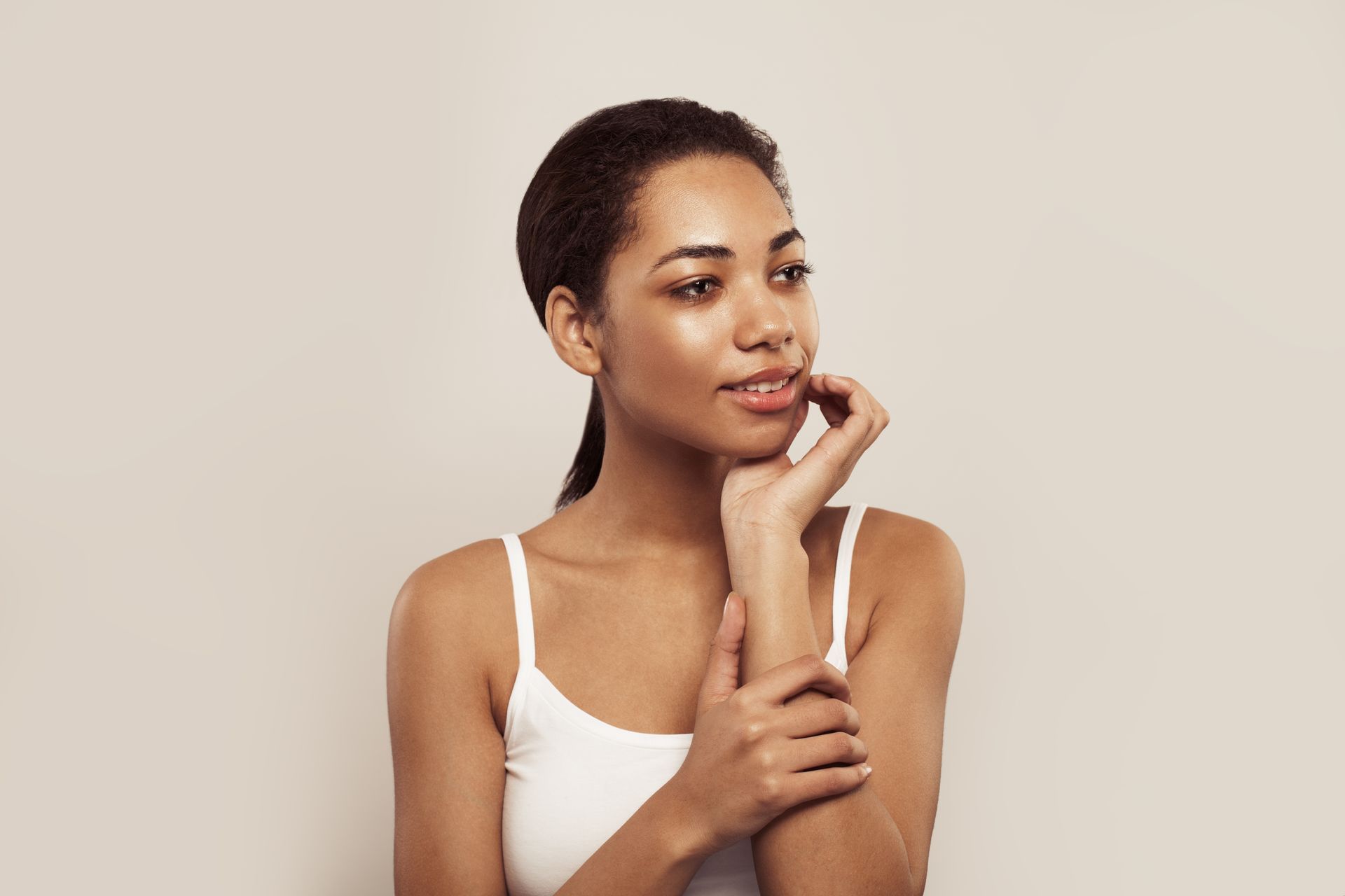 A woman in a white tank top is holding her hand to her face.