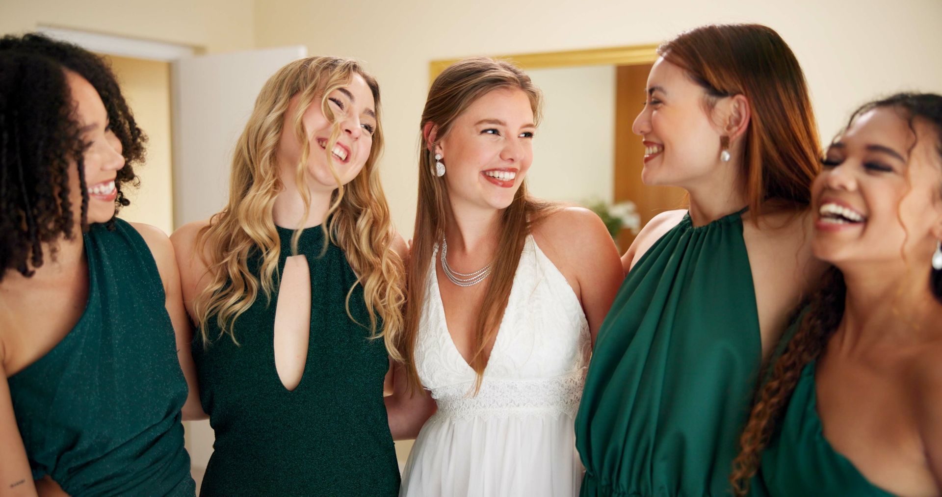 Five young women in formal dresses laughing together in a room.