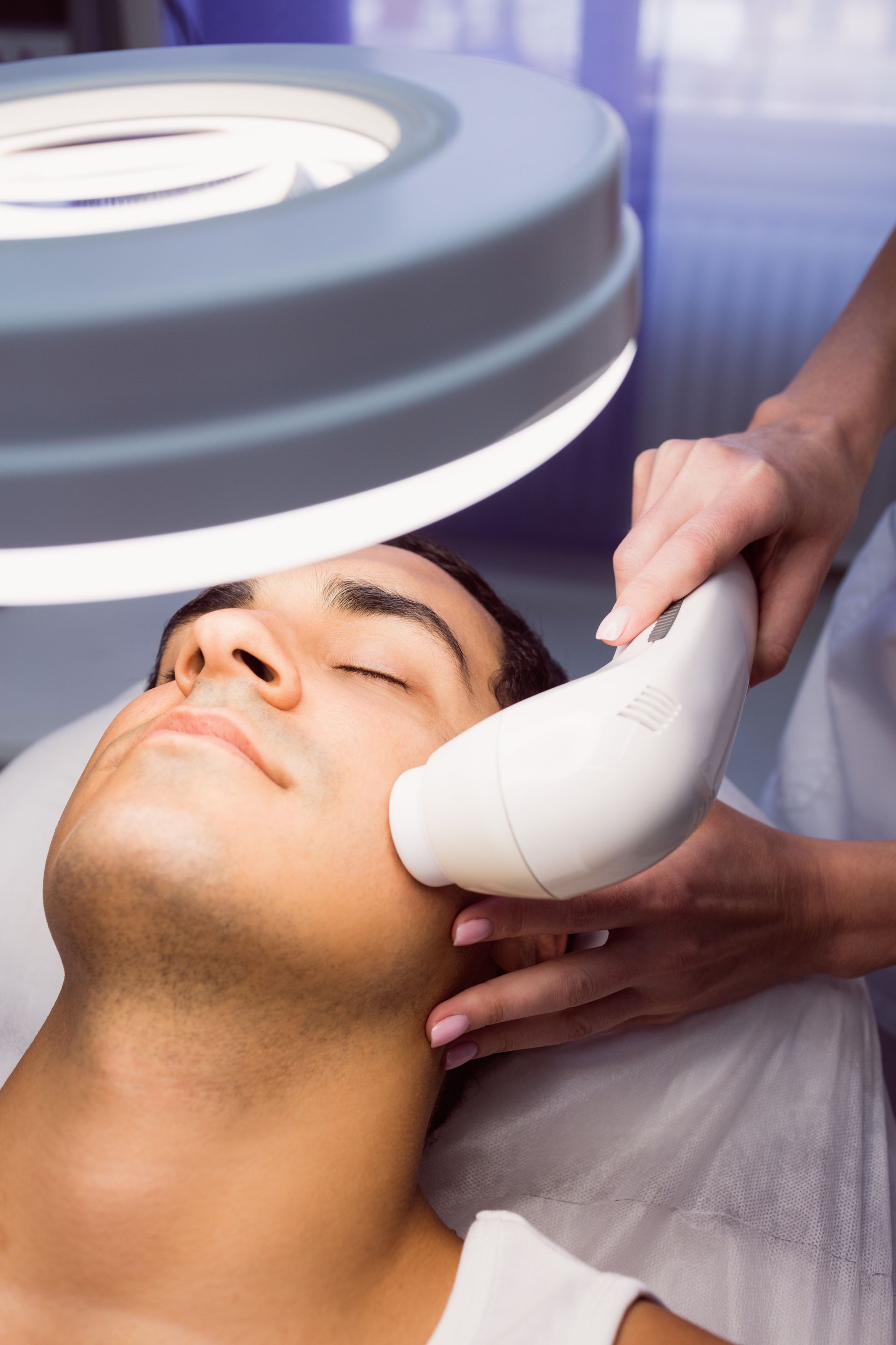 A man is getting a facial treatment under a magnifying glass