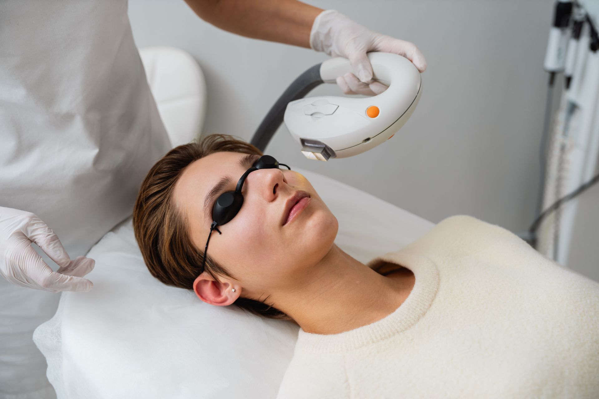 Woman receiving laser facial treatment, wearing protective eyewear, in a clinic.