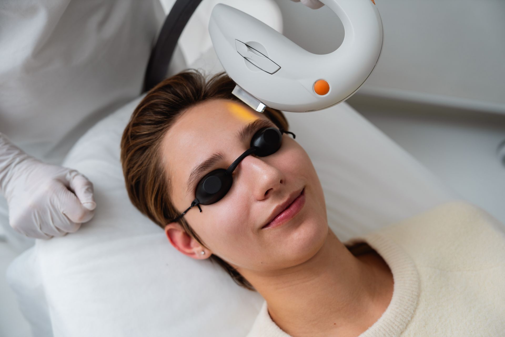 A person wearing protective goggles receives light-based cosmetic skin treatment on their forehead.