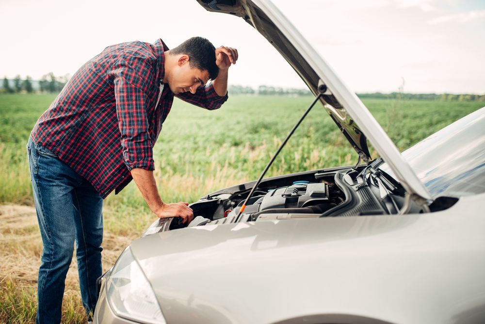 A man is looking under the hood of a broken down car.